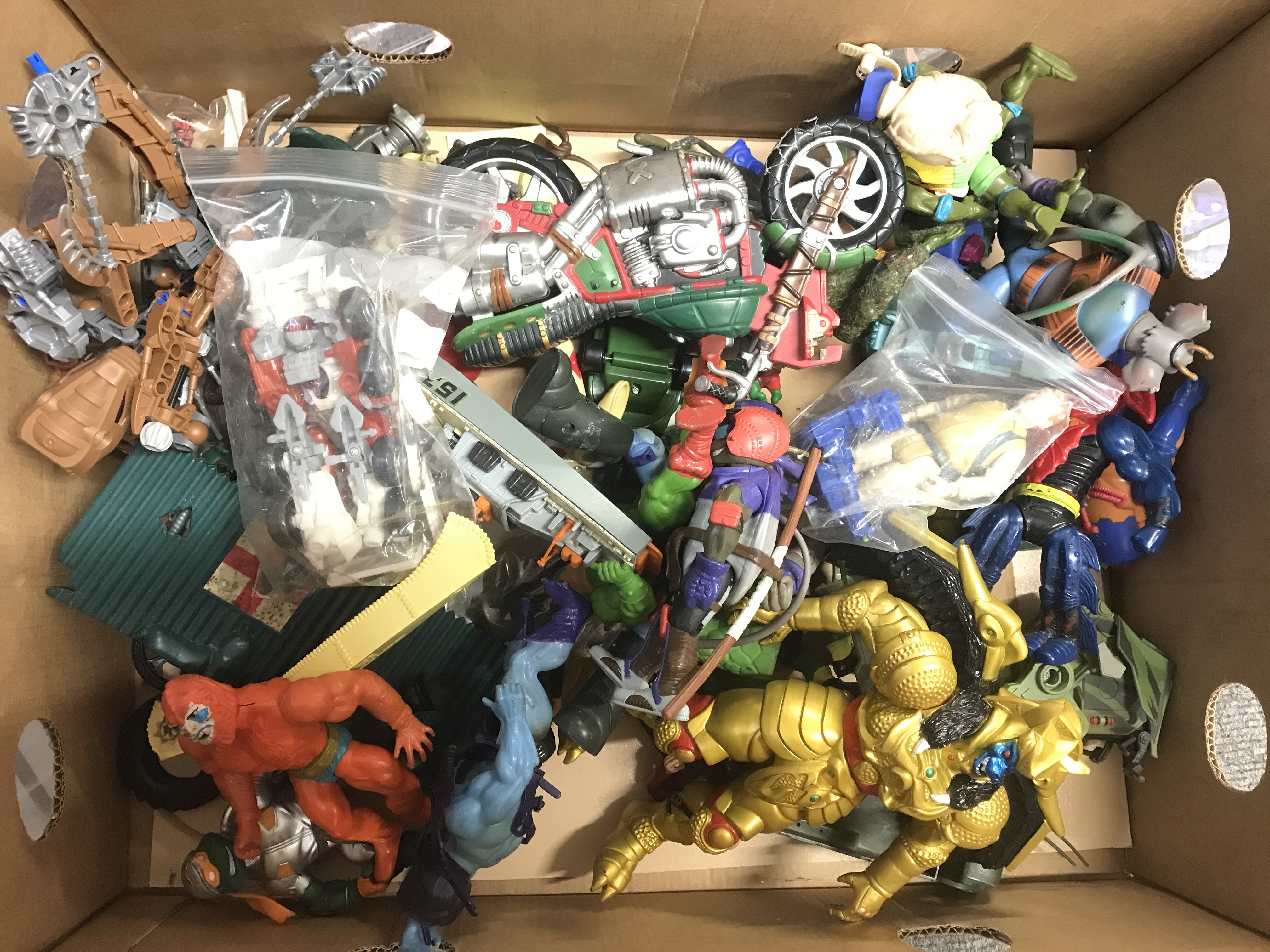 A Box Containing Various Toy/Figures Including Masters Of The Universe. Biker Mice. Turtles. Power Rangers Etc. No Reserve.