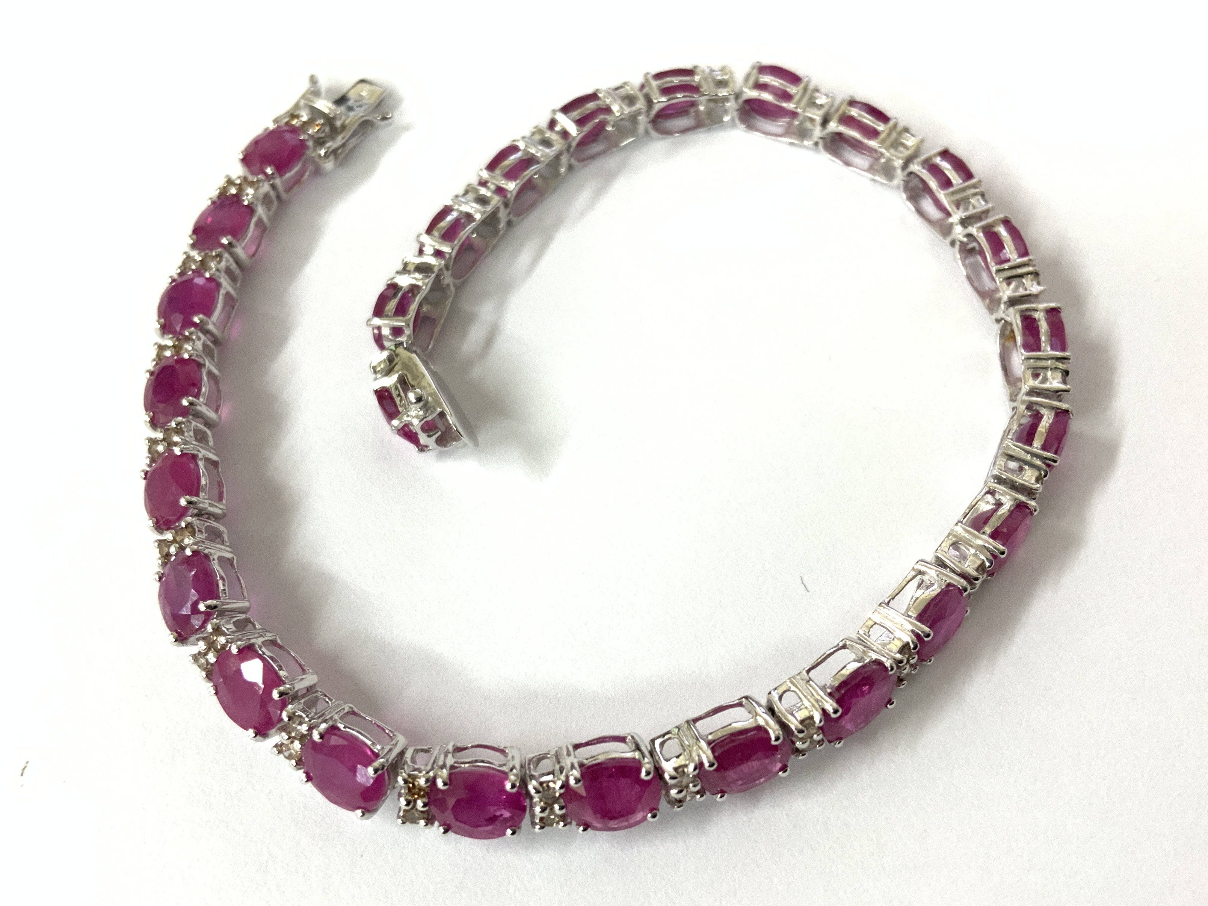 18ct white gold line bracelet set with oval rubies and RBC diamonds, with an open box clasp and double safety catch, boxed. Rubies 11.38ct. Diamonds 0.50ct. Postage category A