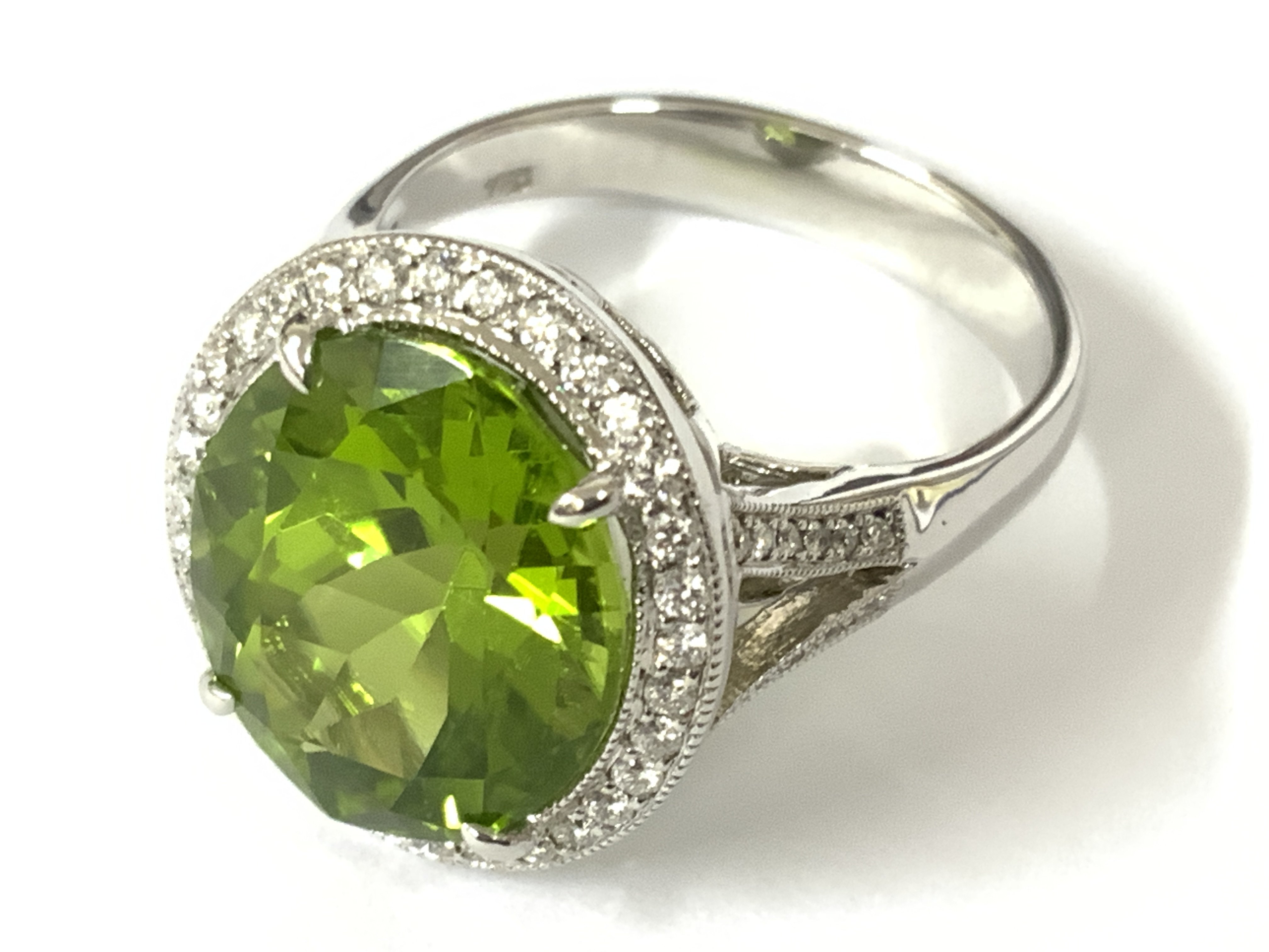 18ct white gold large oval peridot and RBC diamond cluster ring with diamonds to the set split shoulders. Peridot 7.02ct. Diamonds 0.28ct. Approx ring size N/O. Postage category A
