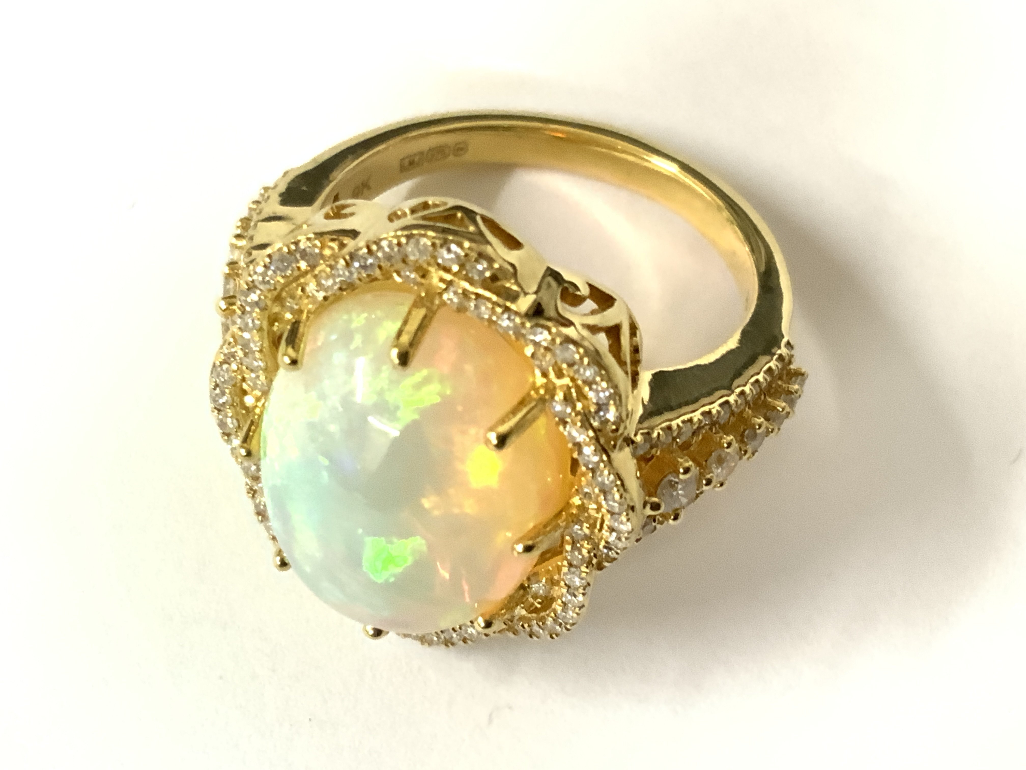 9ct yellow gold ring set with an oval cabochon opal within a twist style diamond surrounded by RBC, with further diamonds to the shoulders. Opal 6.85ct. RBC diamonds 0.59ct. Approx ring size O/P. Postage category A