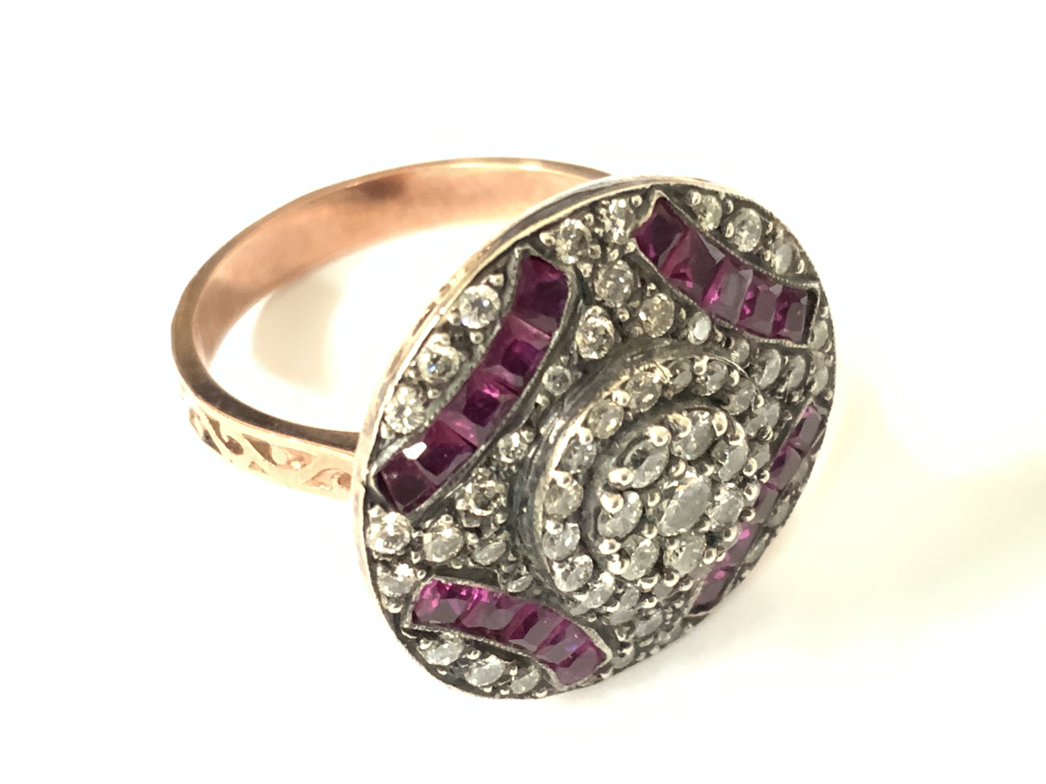 8ct rose gold art deco style round shaped dress ring set with step cut rubies and brilliant cut diamonds. Rubies 0.48ct approx. Diamonds 1.00ct approx. Approx ring size N/O. Postage category A