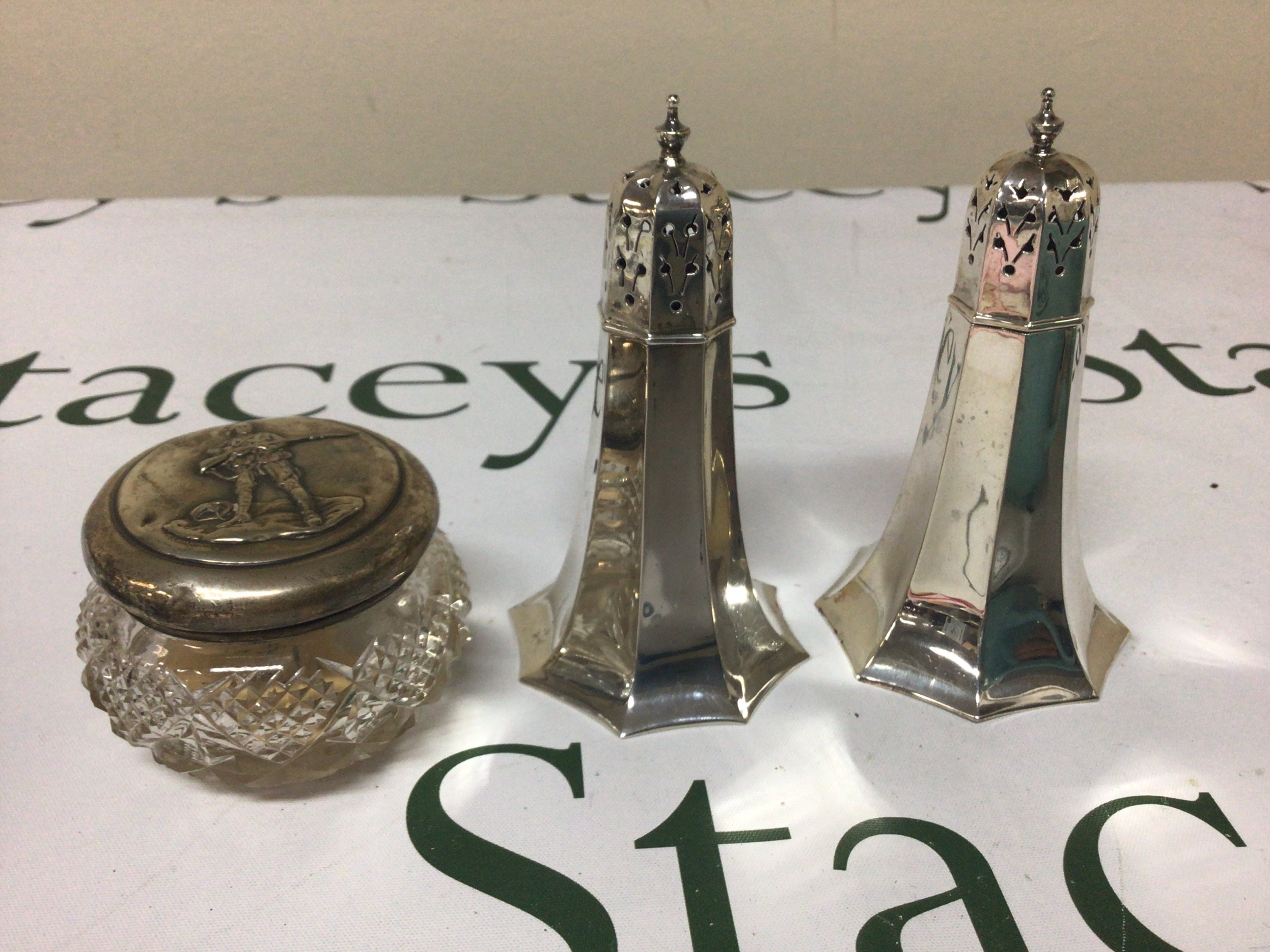A pair of quality silver condiments with octagonal tapering cylinders Sheffield hallmarks weight approximately 170g and a silver topped jar decorated with a North American Indian. (3)