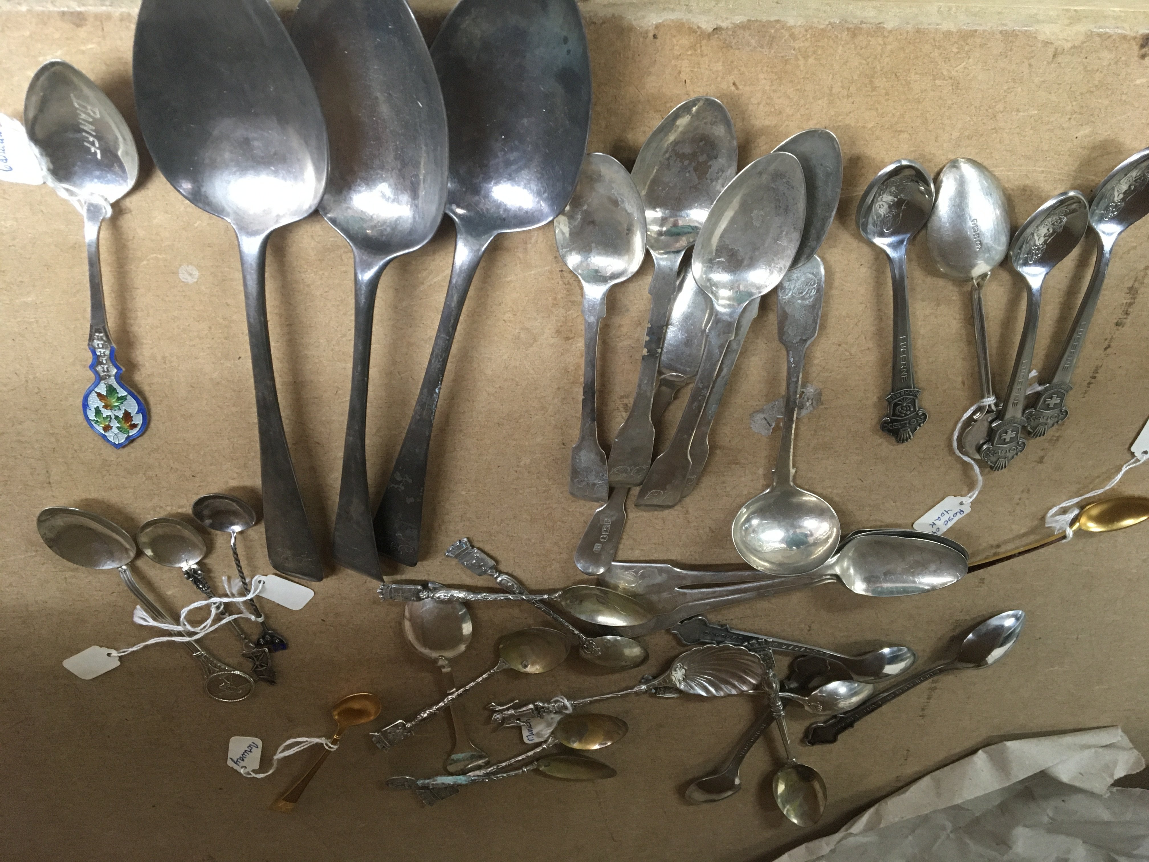 A collection of various spoons including silver , enamel and plated .