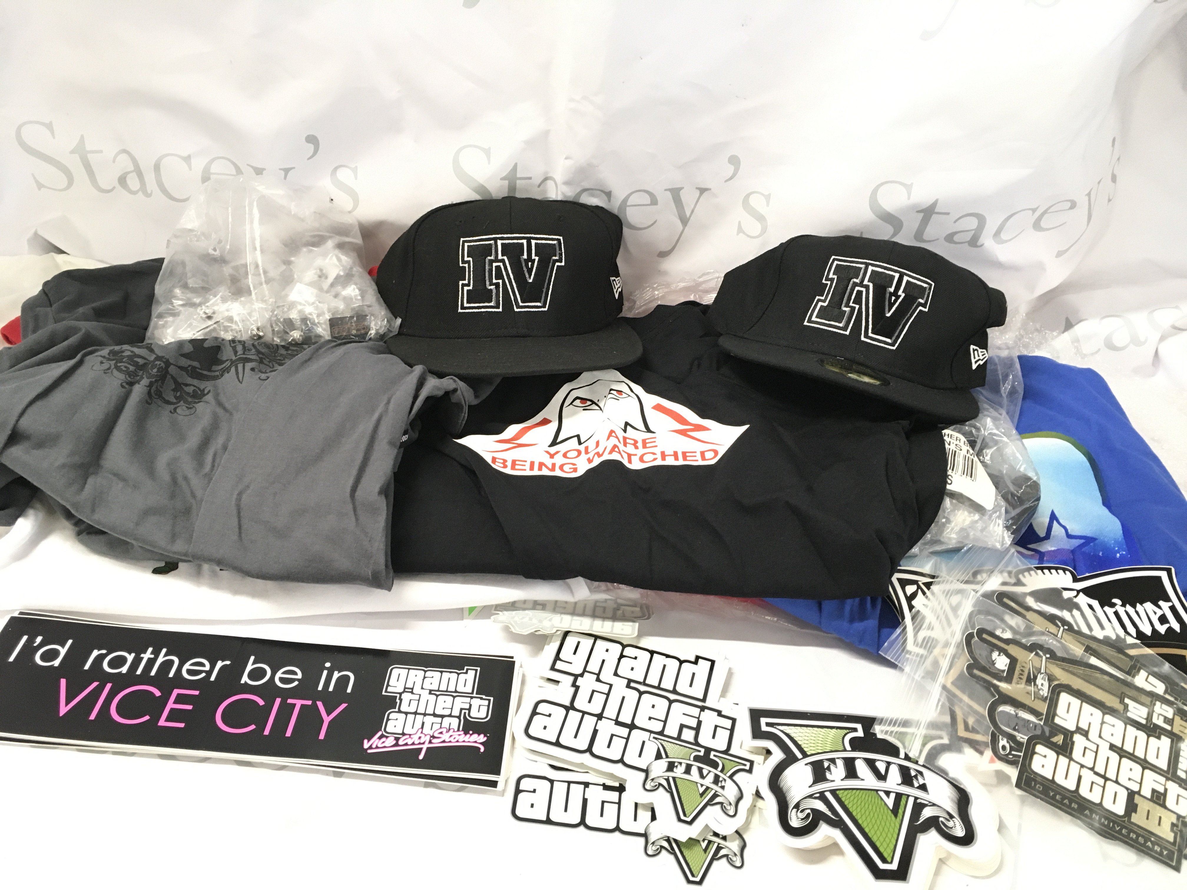A Collection of Rock Star Games Grand Theft Auto Promotional Items Including Stickers. T-Shirts. Caps. Pin Badges. Etc.