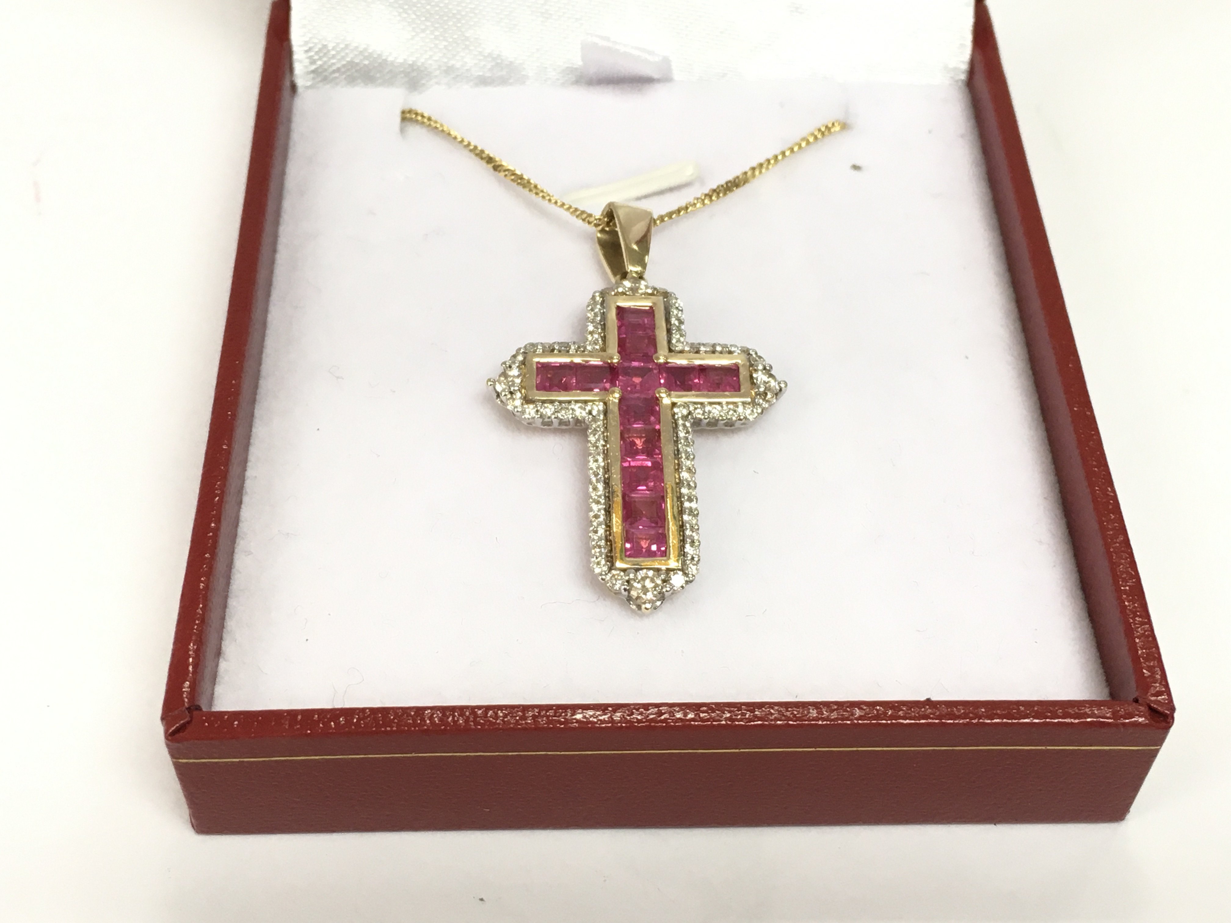 A 14ct yellow and white gold cross pendant set with square cut rubies and RBC diamonds on a gold plated silver chain. Rubies approx 1.80ct and diamonds approx 0.75ct. Approx 9.4g. Shipping category A.