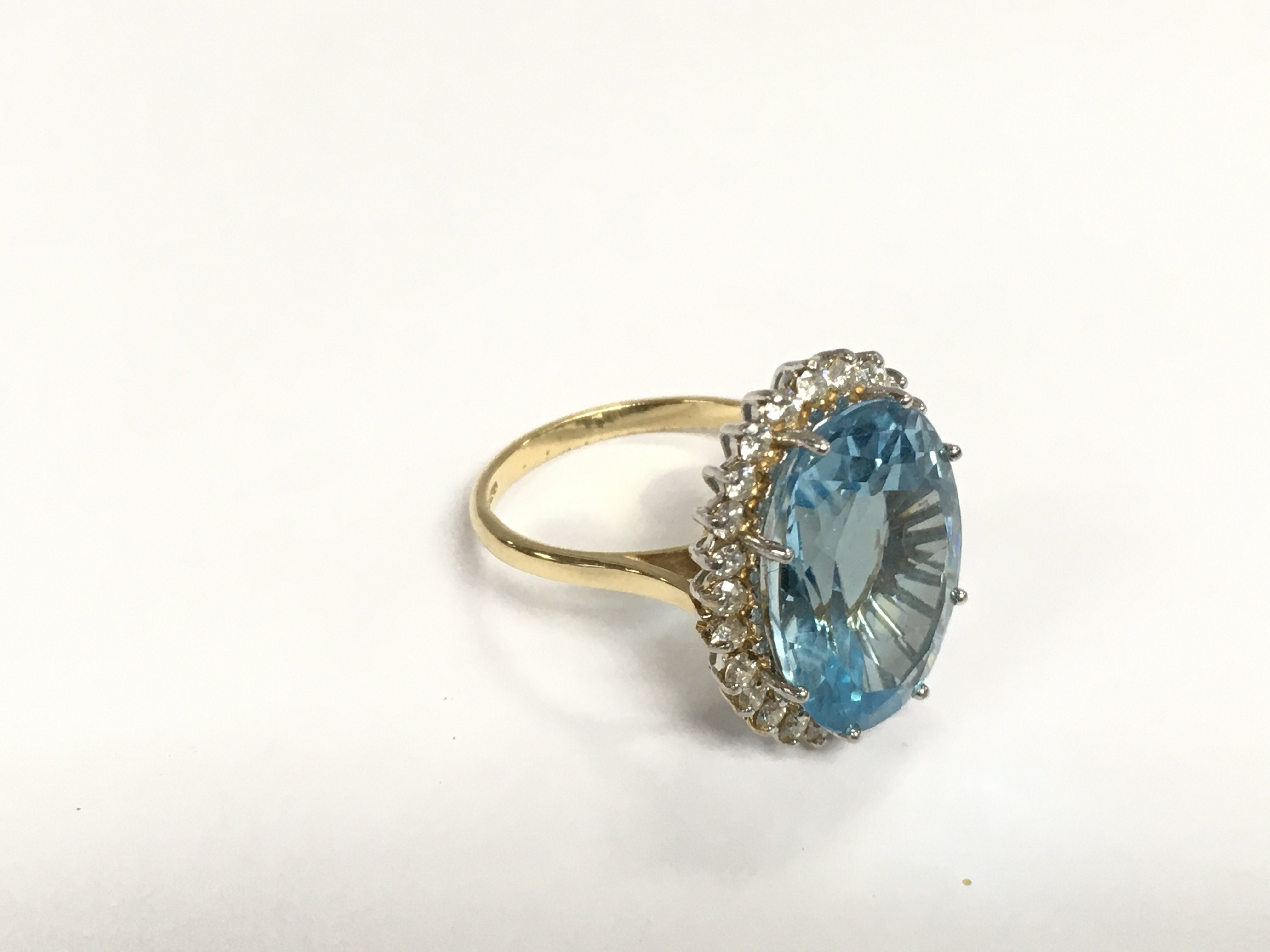 An 18ct white and yellow gold ring set with a large oval faceted blue topaz surrounded by RBC diamonds. Topaz approx 10.00ct, diamonds approx 0.80ct. Approx 8g and approx size N. Shipping category A.