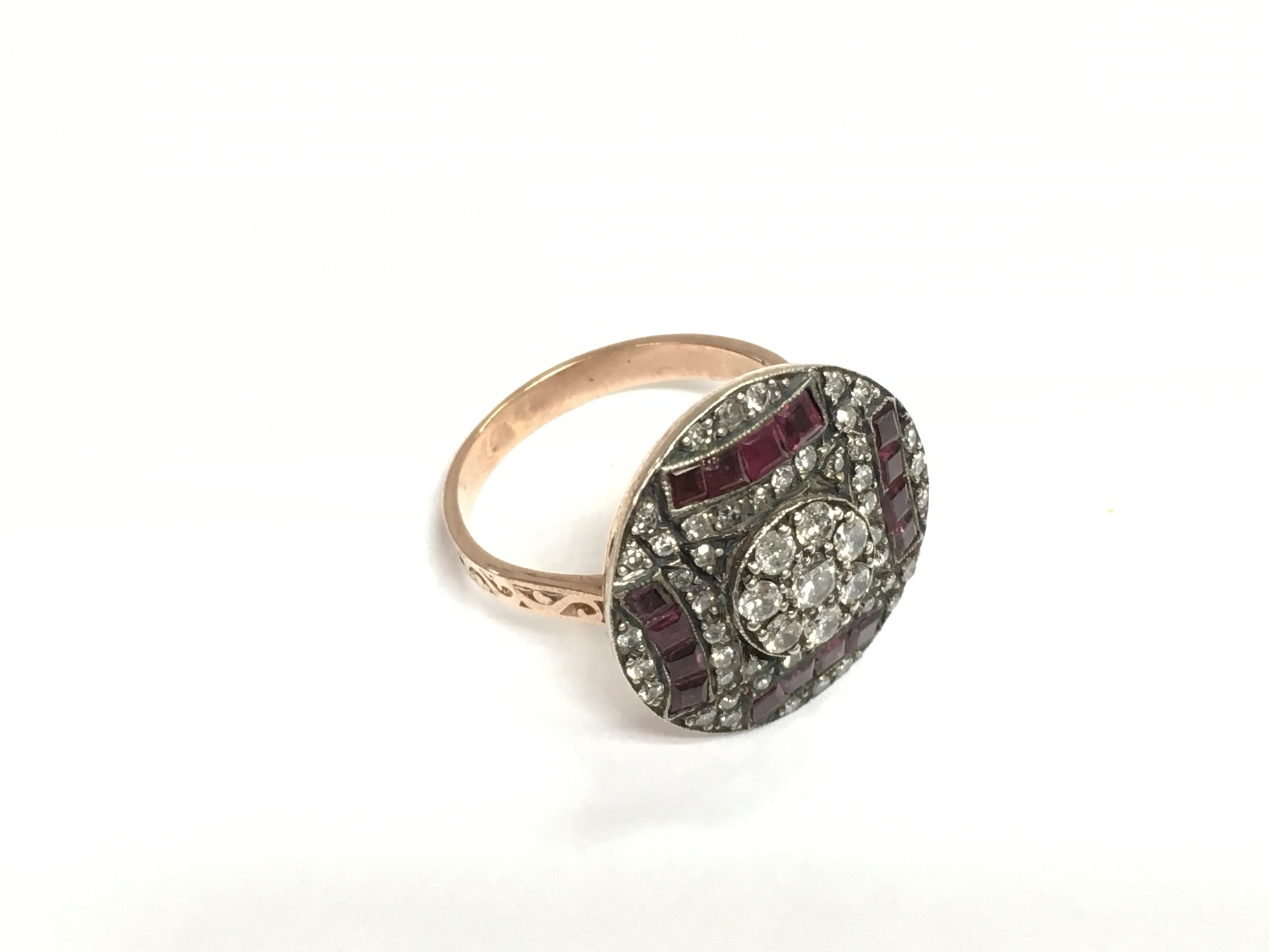 An unhallmarked rose gold silver topped circular A Deco style ring set with calibre cut rubies and BC diamonds with patterned shoulders. Diamonds approx 0.90ct, rubies approx 0.75ct. Approx 6.3g and approx size N. Shipping category A.