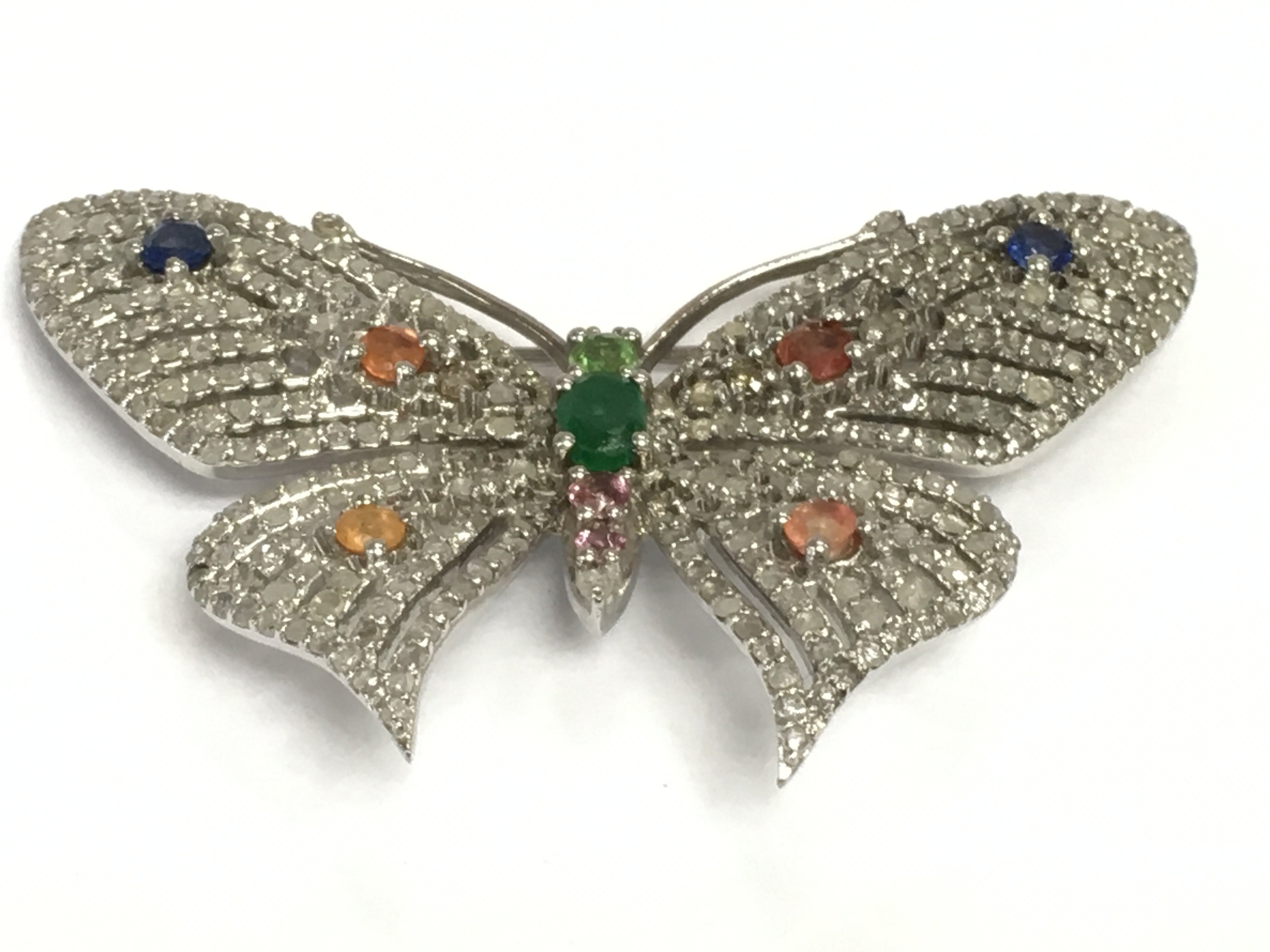 A stylish silver butterfly brooch/pendant set with emeralds, vari coloured sapphires and several diamonds. Diamonds approx 1.86ct, sapphires approx 1.21ct, emeralds approx 0.20ct. Approx width 5.5cm. Shipping category A.