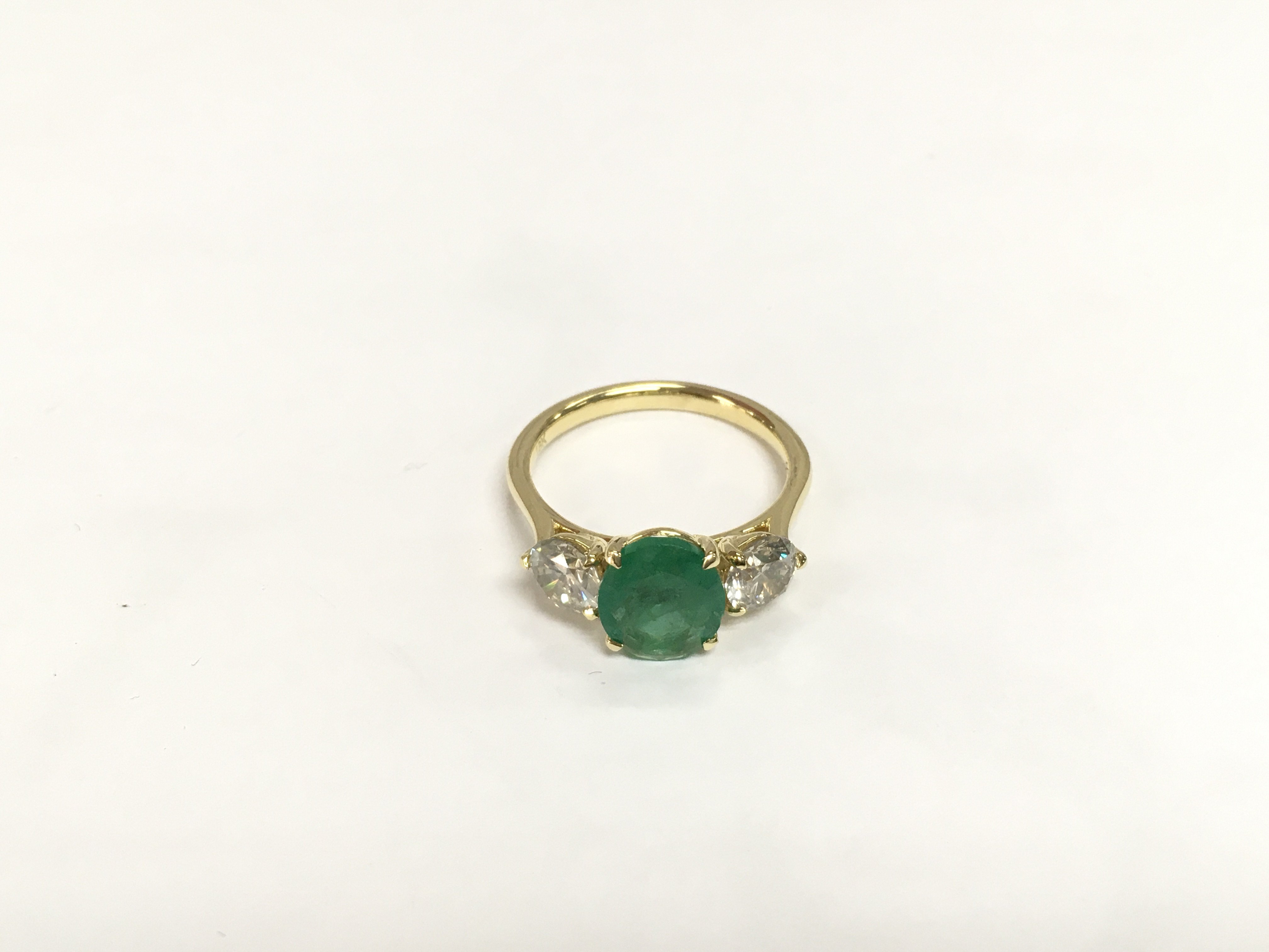An 18ct yellow gold trilogy ring set with an oval emerald flanked by RBC diamonds. Emerald approx 1.72ct, diamonds approx 1.23. Approx 3.8g and approx size M-N. Shipping category A.