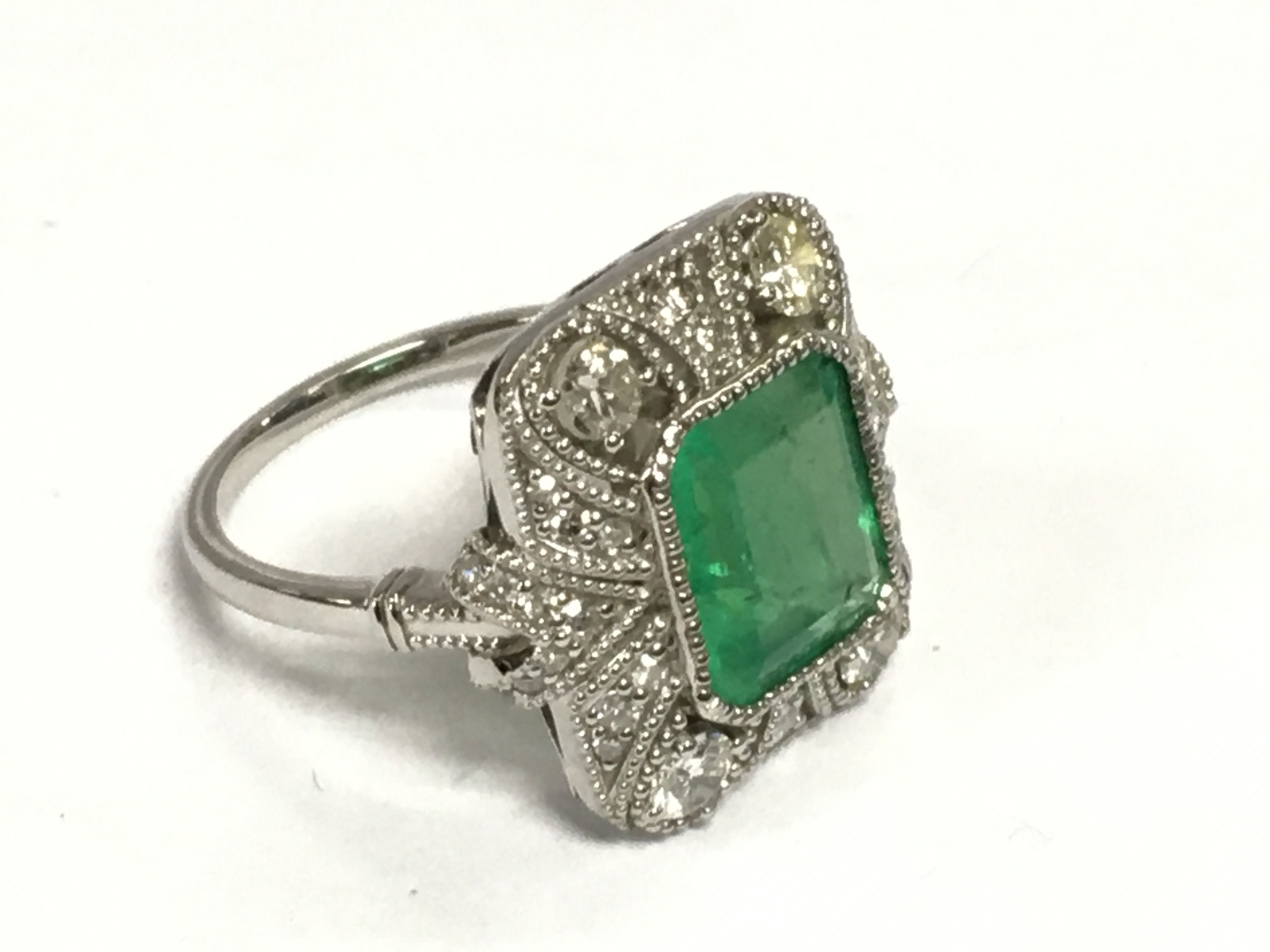 A platinum Edwardian style dress ring set with emeralds and diamonds with millegrain and filigree scroll detailing. Step cut emerald approx 2.52ct, RBC and eight cut diamonds approx 0.82ct. Approx 7g and approx size L. Shipping category A.