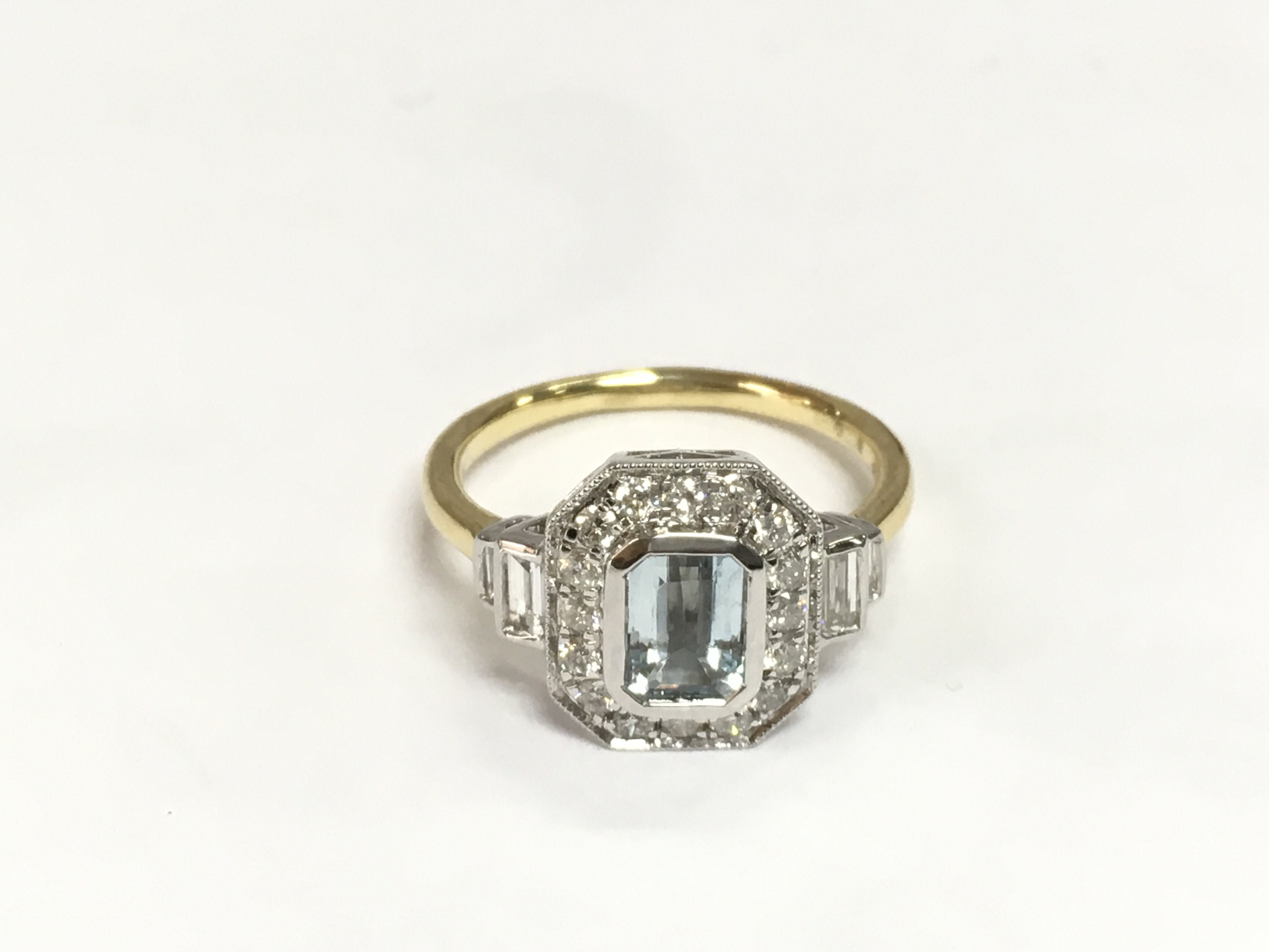 An 18ct yellow and white gold Art Deco style dress ring set with a step cut aquamarine with baguette and RBC diamonds. Aquamarine approx 0.82ct, diamonds approx 0.60ct. Approx 4.5g and approx size O. Shipping category A.