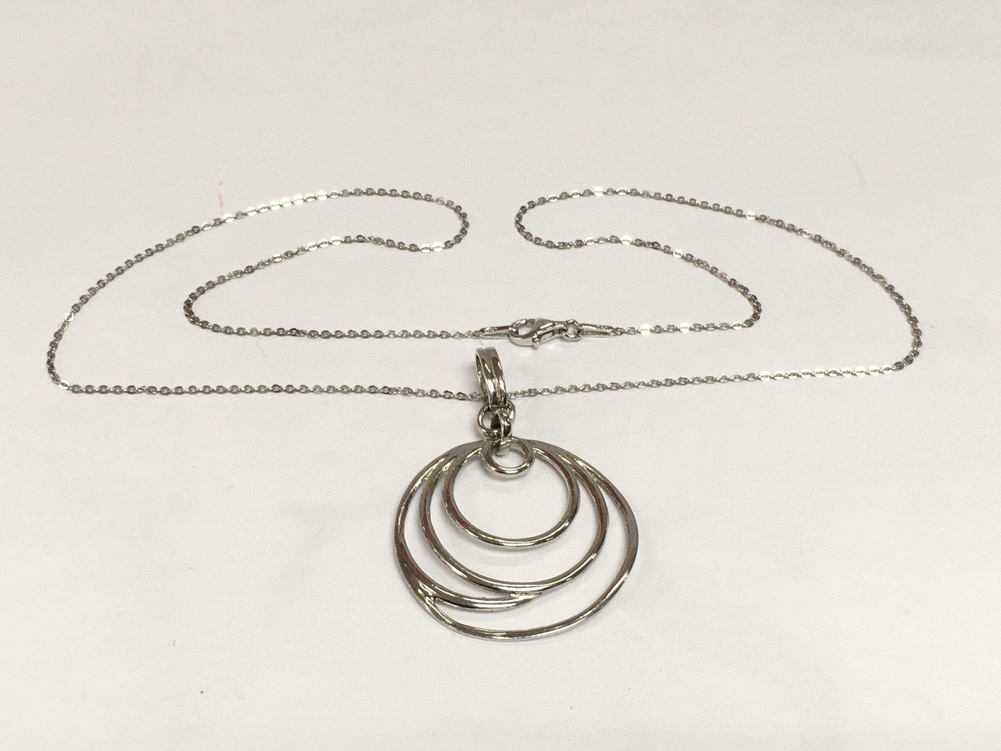 A circular modern art inspired silver pendant suspended on a silver chain. Shipping category A.