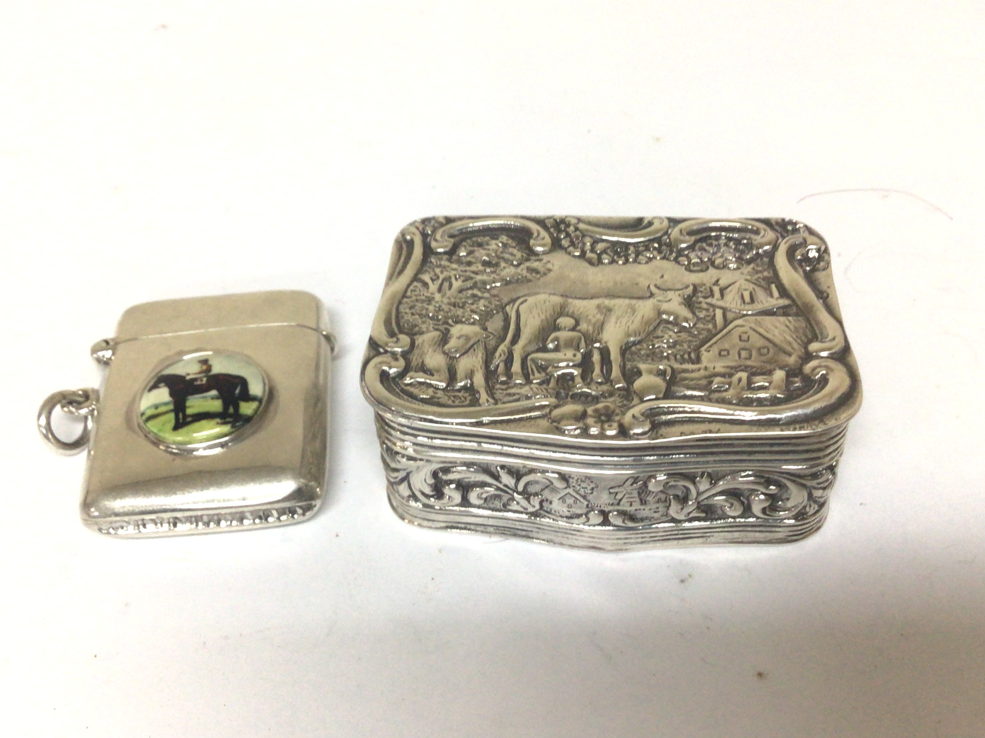 A Continental silver snuff box with Repousse chasing with cattle and rural scene. and a Vesta case with enamel decoration of a race horse (2)