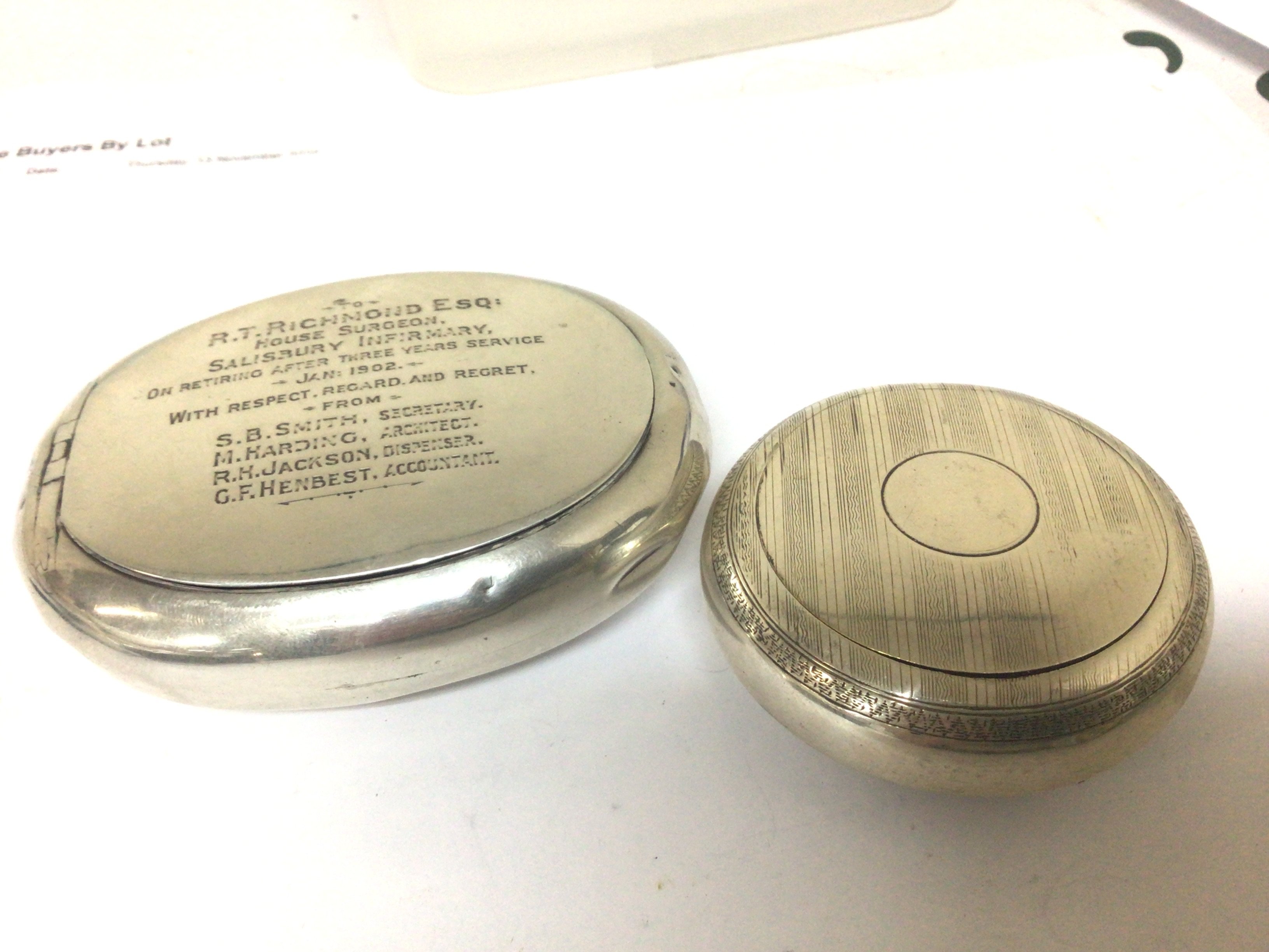 Two silver tobacco boxes one of round shape with engine turned decoration the other with the inscriptions RT Richmond Esq House Surgeon. 1902 (2)