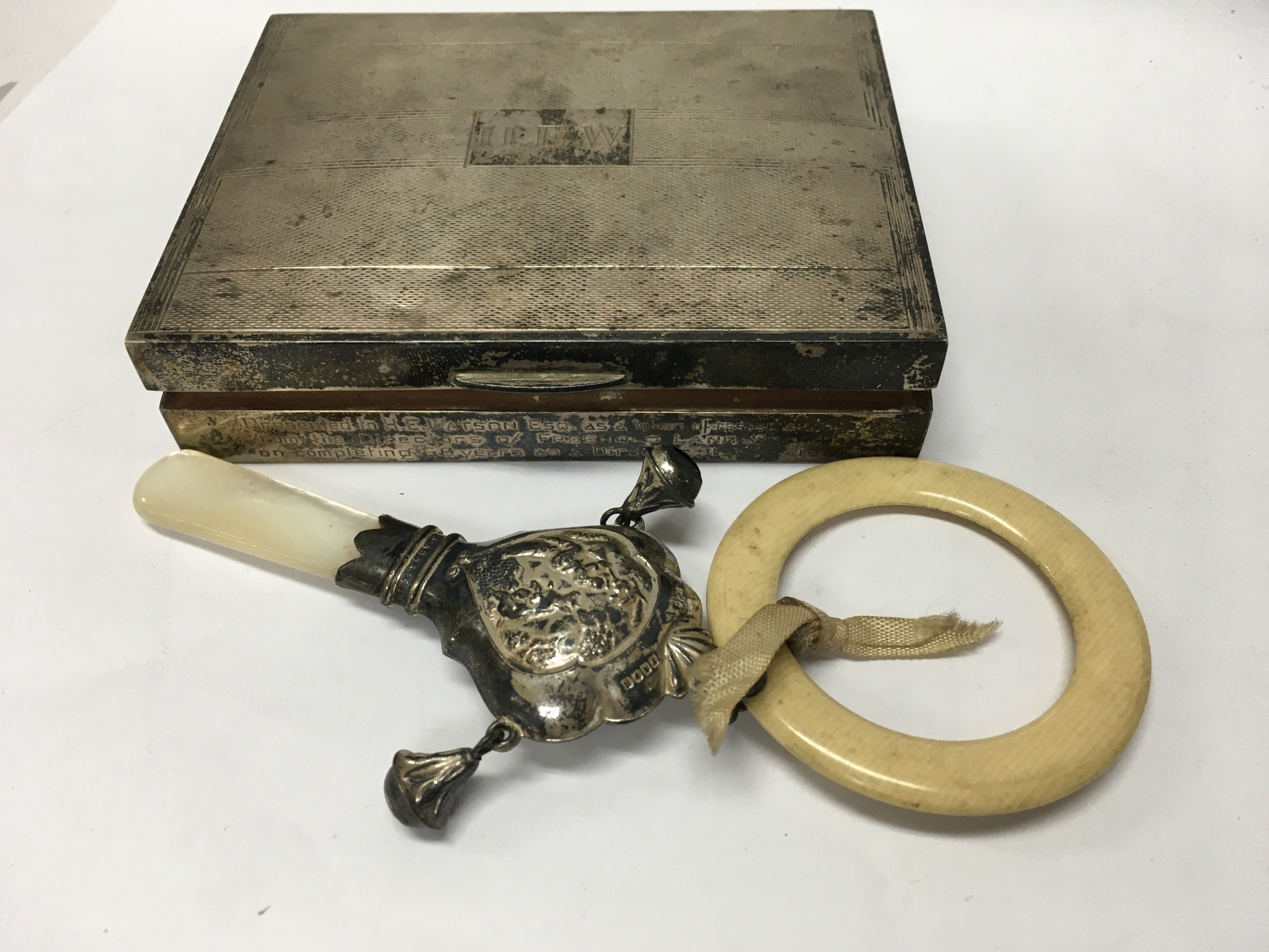 A small silver cigarette box together with a childs rattle.