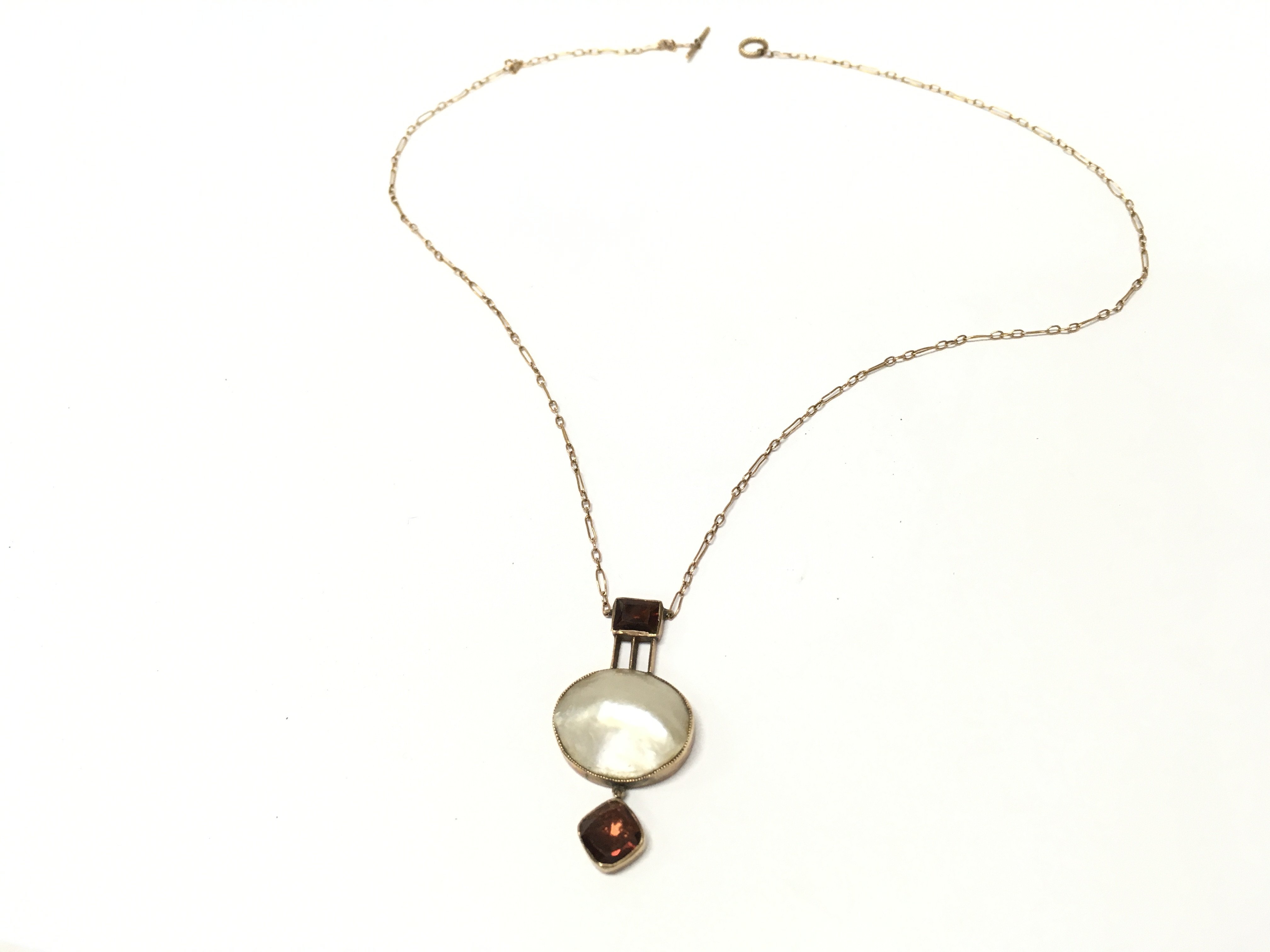 An art deco style necklace with mother of pearl and garnet design . Postage cat a