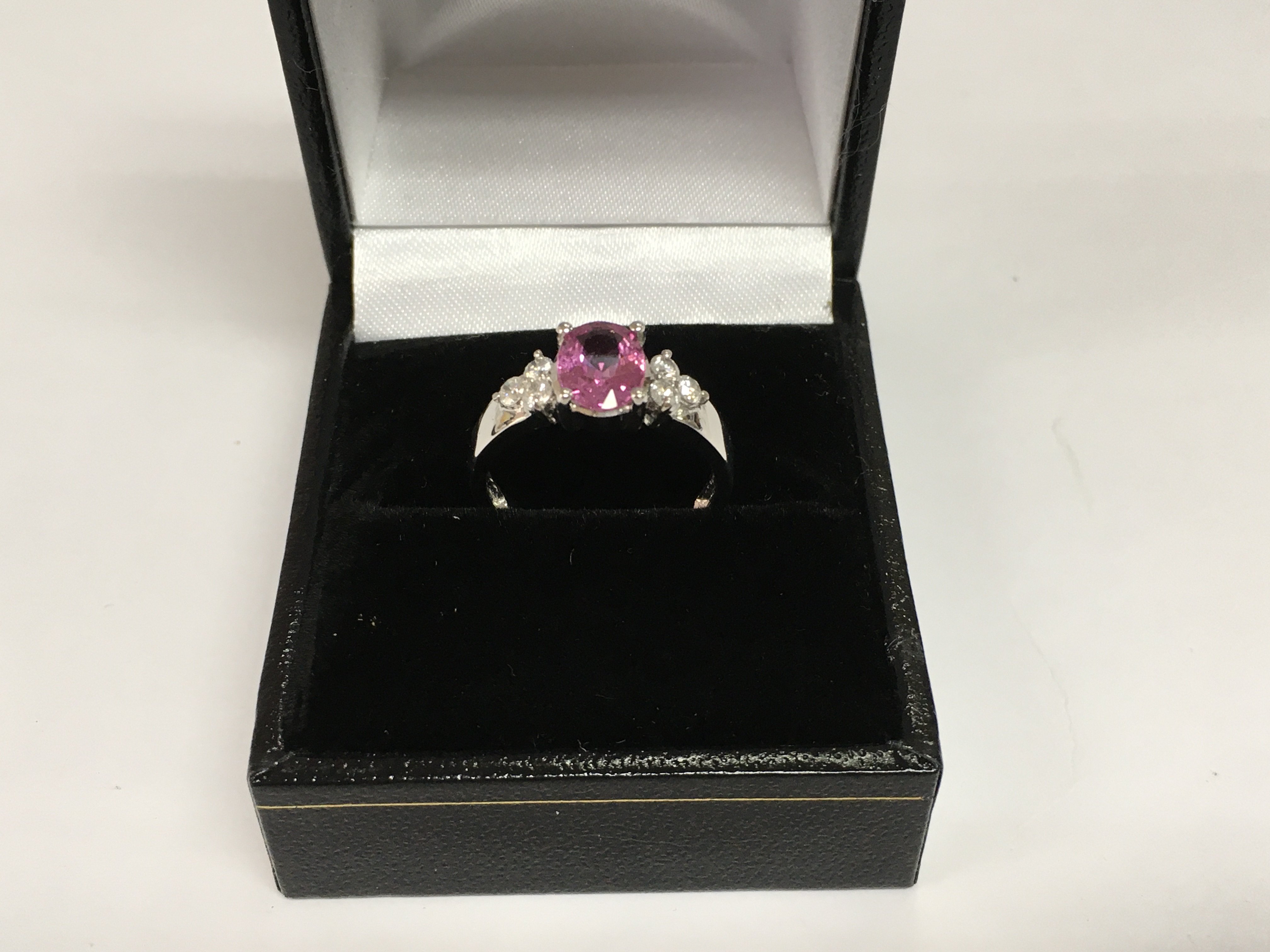 An 18ct white gold trilogy ring set with an oval pink sapphire flanked by six RBC diamonds. Sapphire approx 1.65ct, diamonds approx 0.27ct. Approx 3.2g and approx size L-M. Shipping category A.