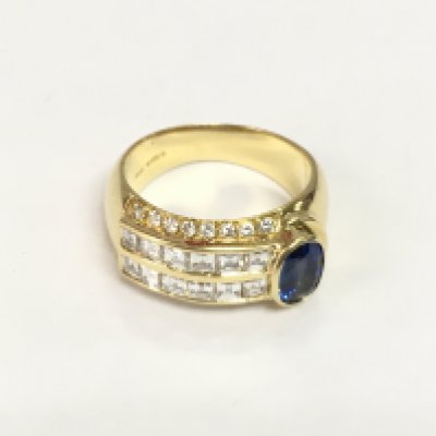 An 18ct yellow gold ring set with an oval sapphire set to one side with square baguette cut and RBC diamonds set to the band. Diamonds approx 1.00ct, sapphire approx 0.70ct. Approx 9.3g and approx size L-M. Shipping category A.