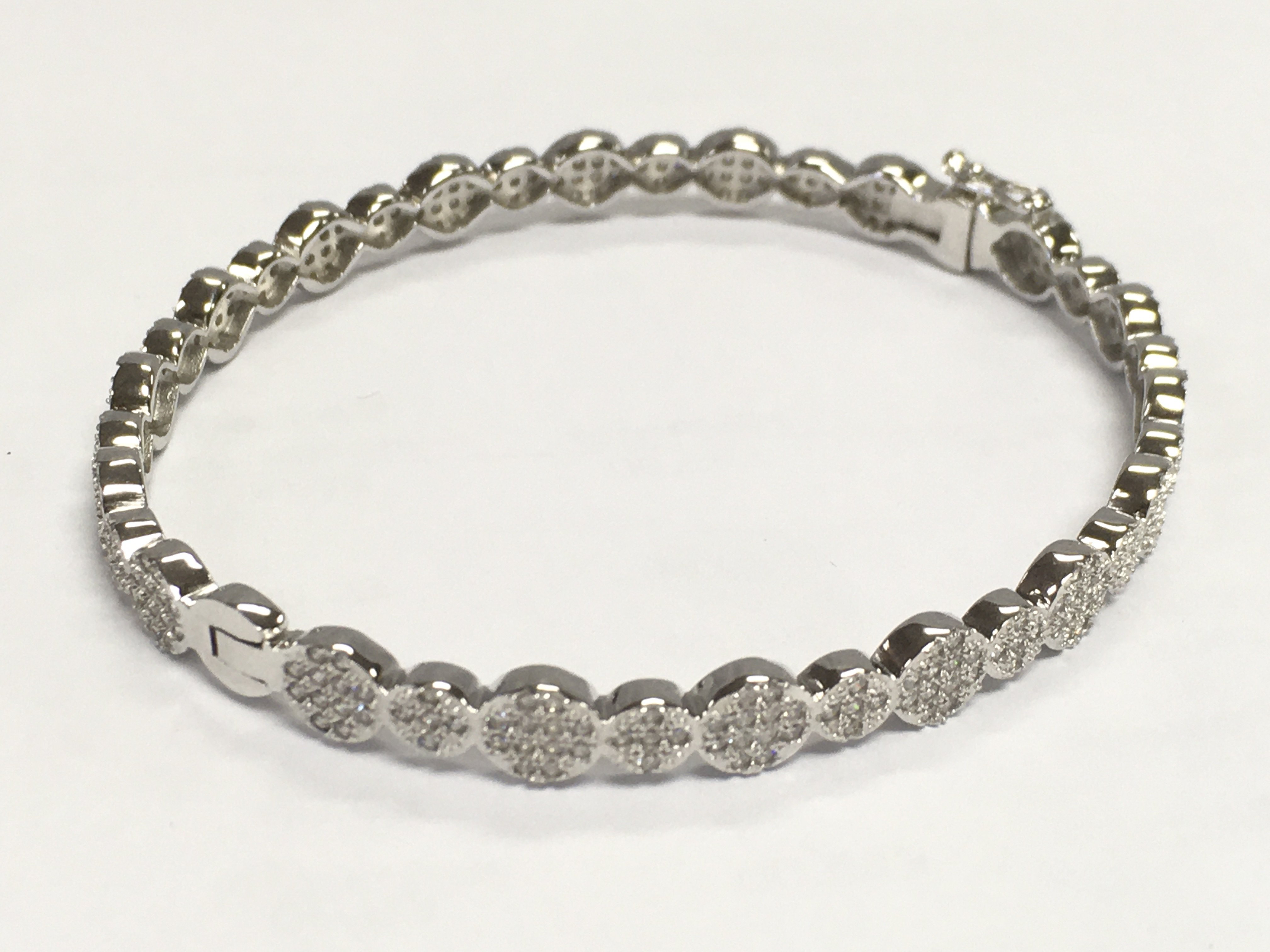 Silver bangle set with clusters of round white cubic zirconia, with hinged opening and safety catch. 13.5g total weight. 