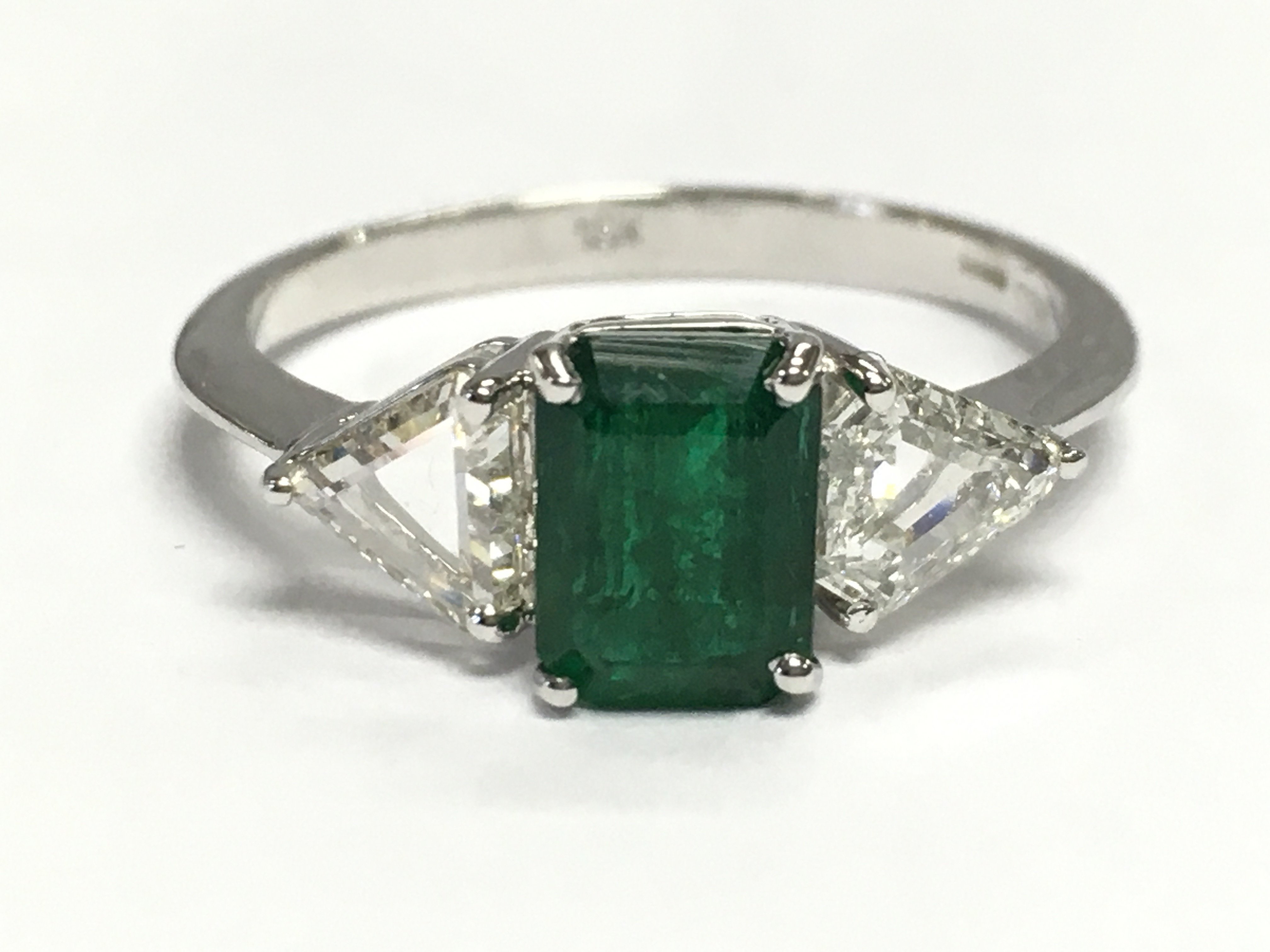 18ct white gold ring set with a rectangular step-cut emerald flanked by trilliant-cut diamonds. Emerald 1.18ct. Diamonds 0.60ct. Size O. 