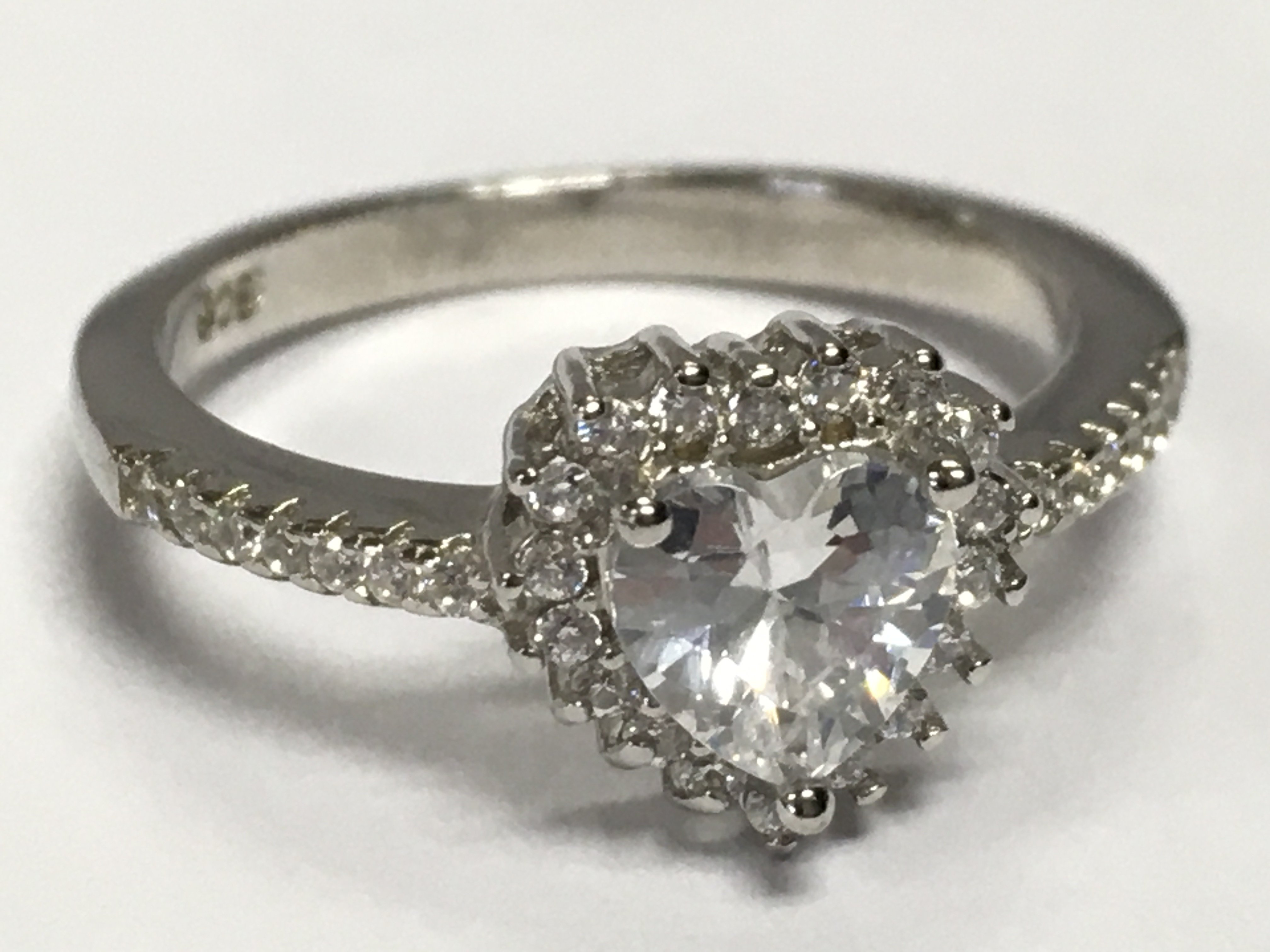 A silver ring set with a central white heart shaped cubic zirconia , with a halo of CZs and CZ shoulders. Size P. 