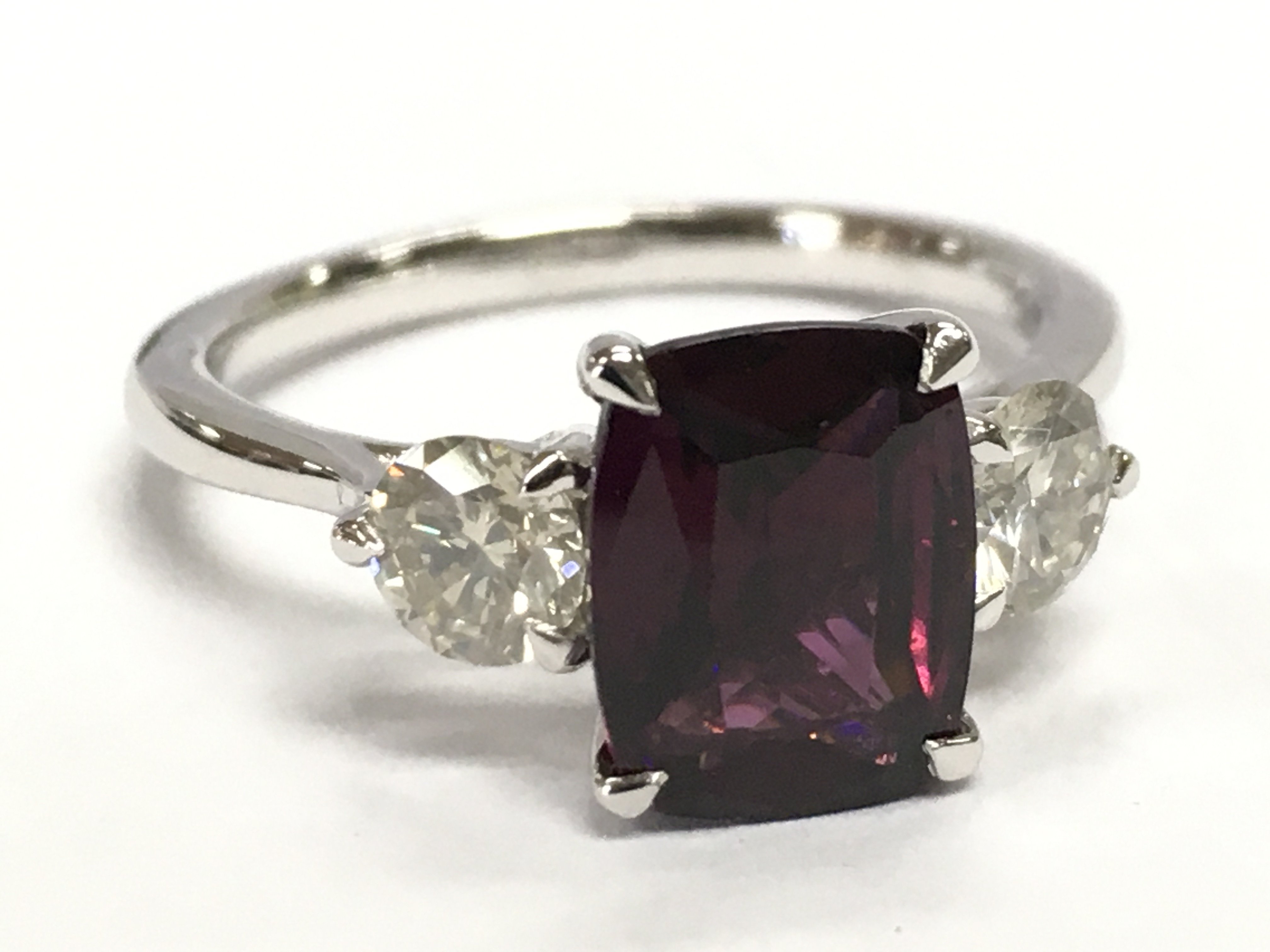 A platinum three stone ring set with a cushion step-cut almandine garnet and 2 RBC diamonds. Garnet 2.36ct, diamonds 0.63ct. Size N.