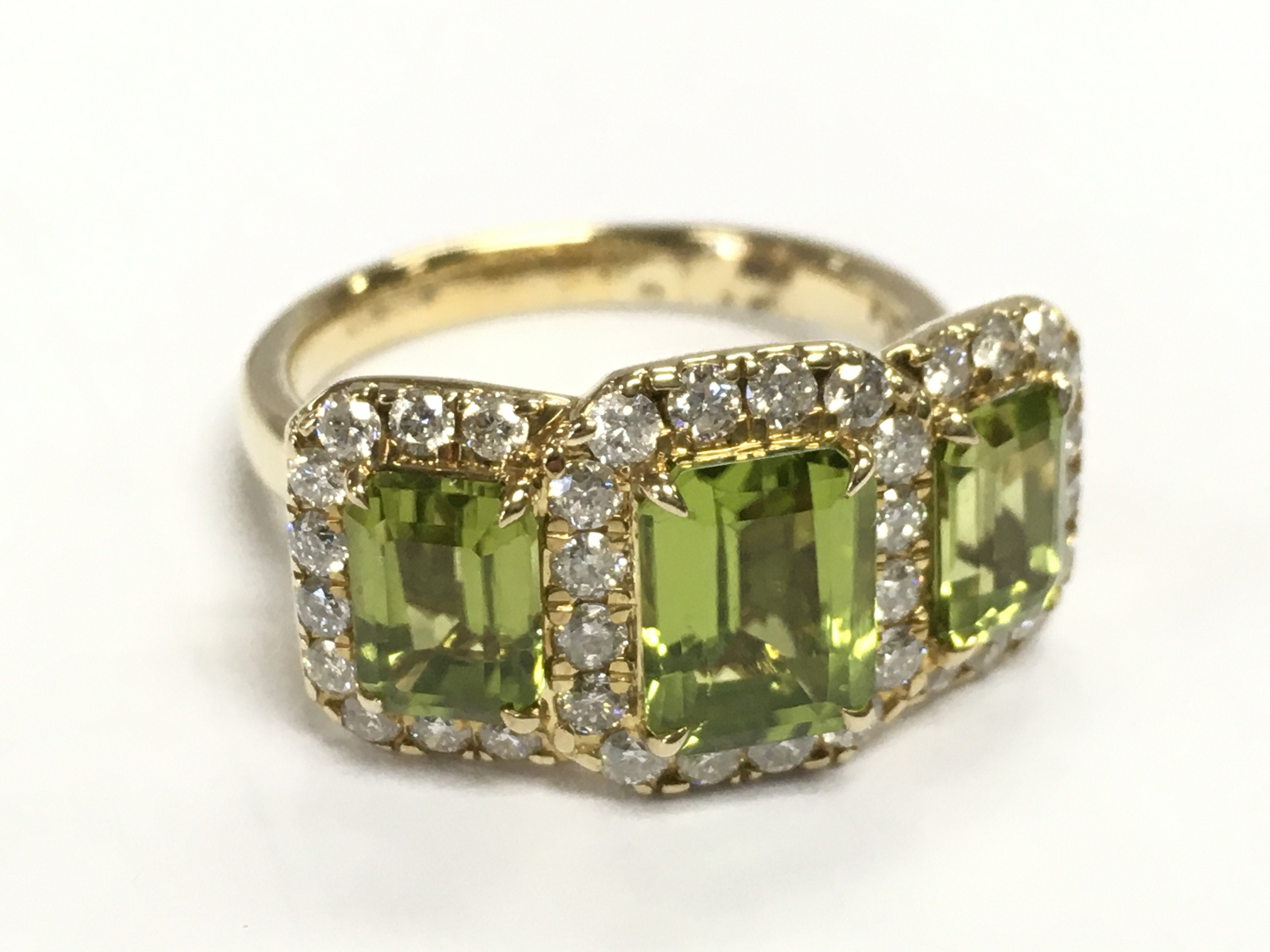 A 9ct yellow gold trilogy ring set with three step cut peridots each surrounded by RBC diamonds. Peridot 3.67ct, diamonds 0.77ct. Size O.