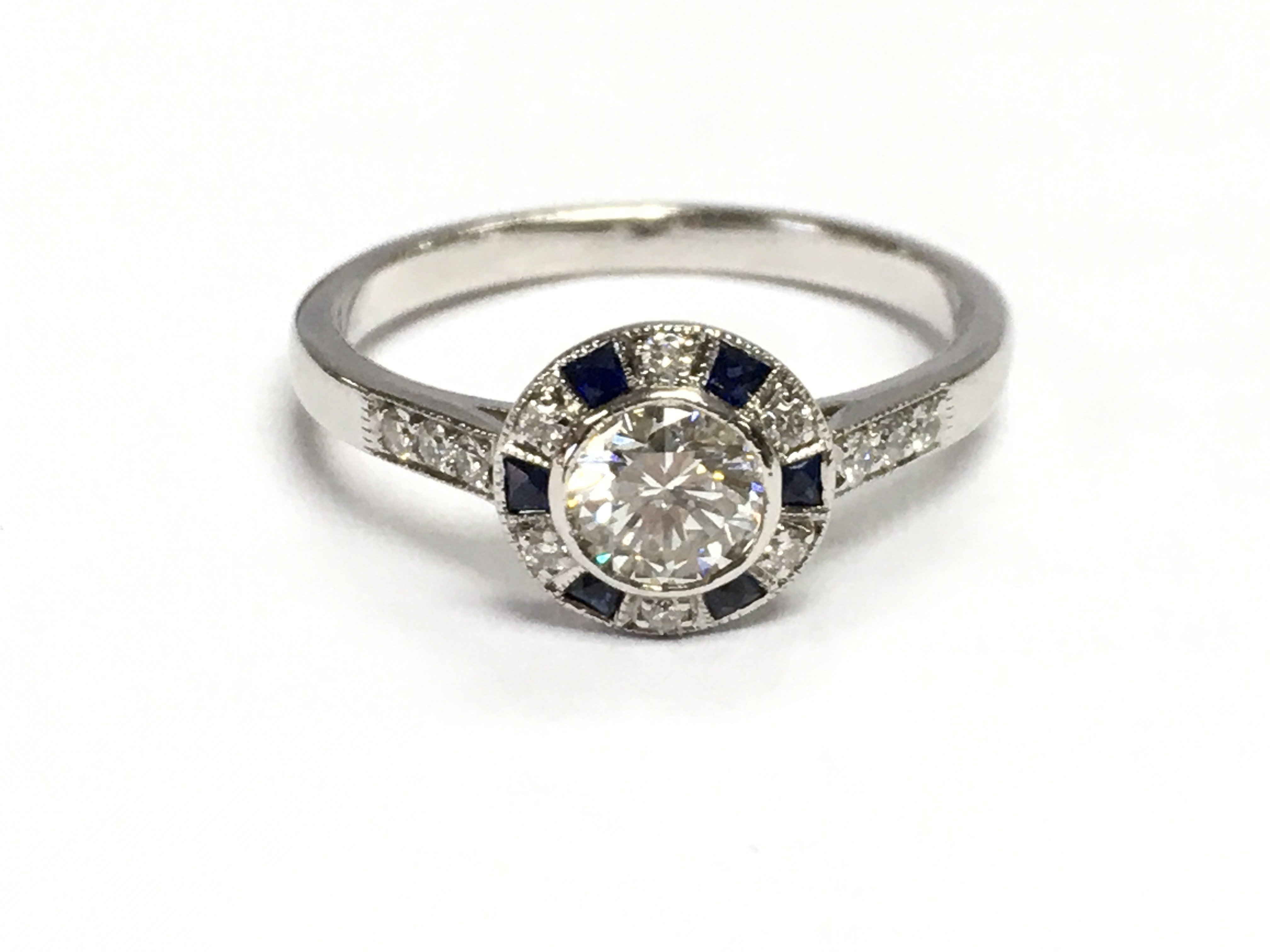 An 18ct white gold target style ring set with a central RBC diamond surrounded by square sapphires and further RBC diamonds, with diamond set shoulders. Diamonds 0.65ct sapphire 0.10ct. Size M/N. 3g total weight.