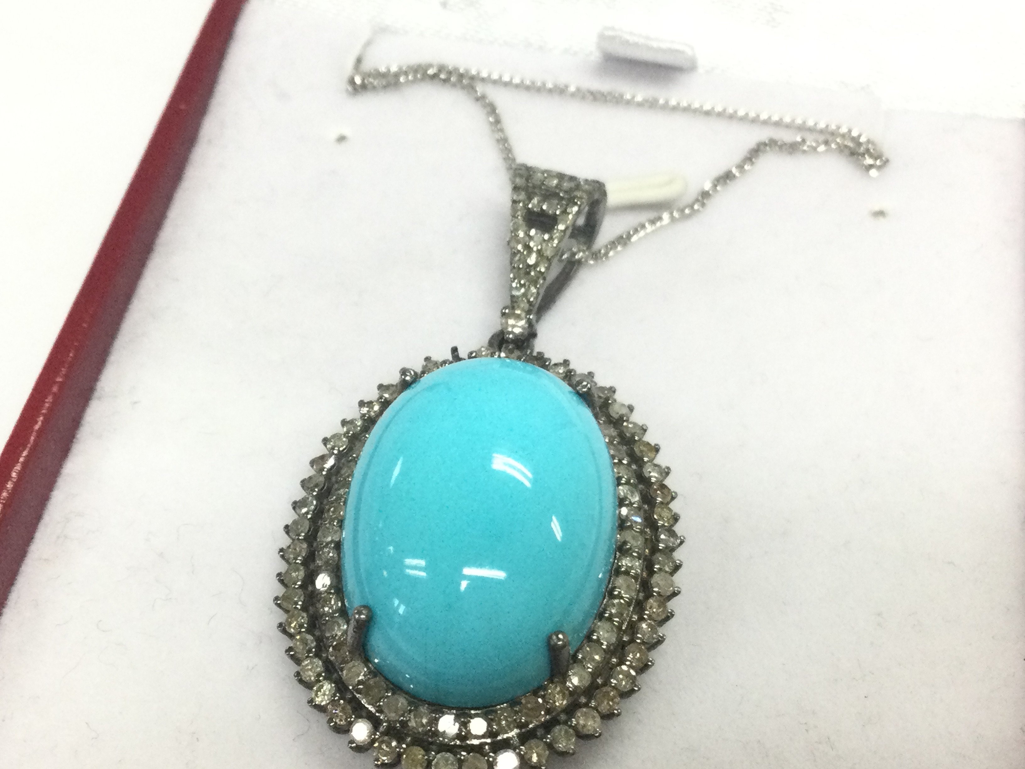 An oval pendant in white metal set with a large oval cabochon turquoise and double halo set with R/C diamonds , with diamond set bale on a silver chain. Boxed. Turquoise 17.21ct. diamonds 1.87ct. 
