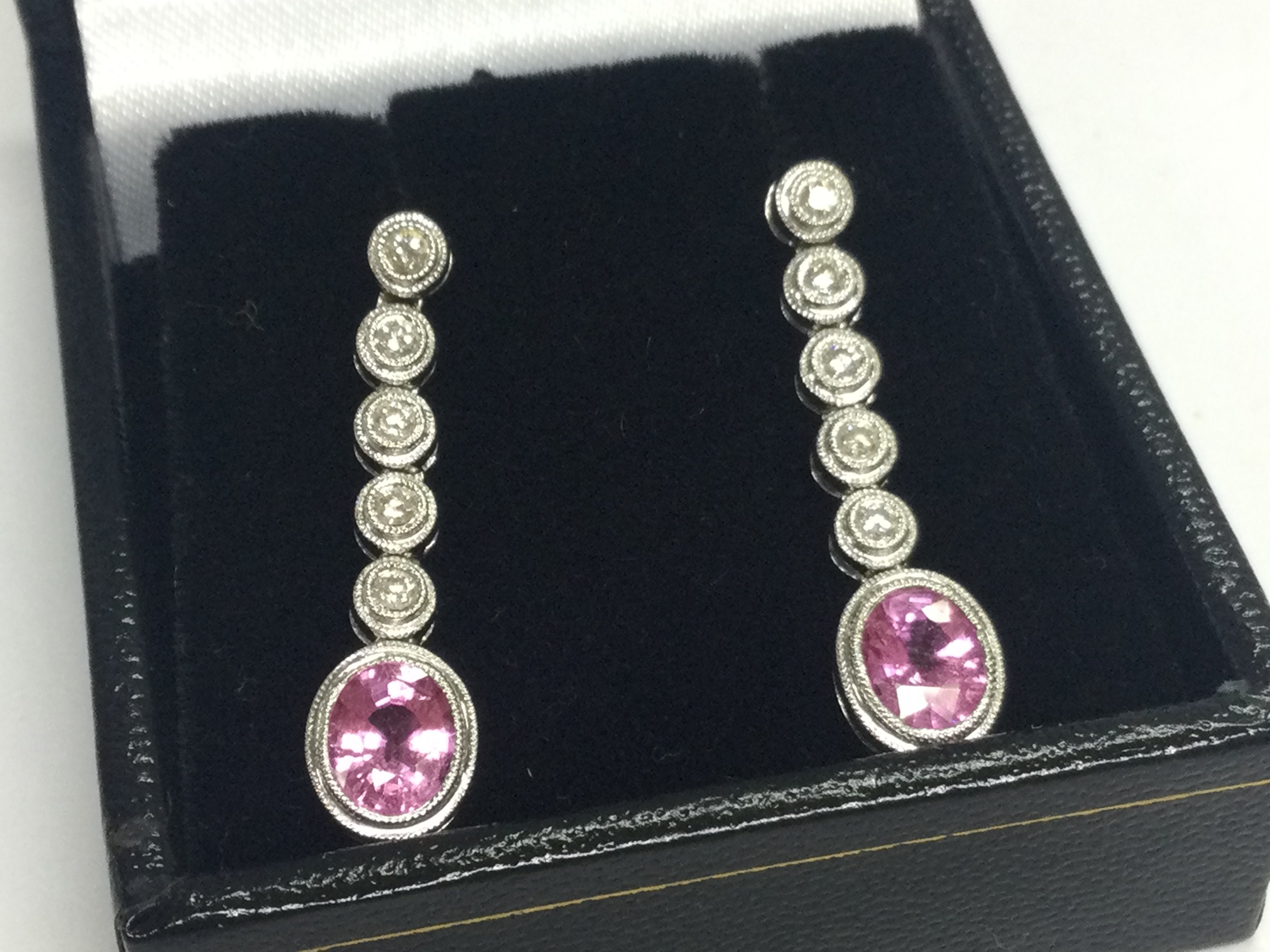 Pair of 18ct white gold drop earrings set with oval pink sapphires and RBC diamonds with millgrain detailing. Boxed. Pink sapphires 1.00ct approx. Diamonds 0.25ct approx . Total weight 4.3G 