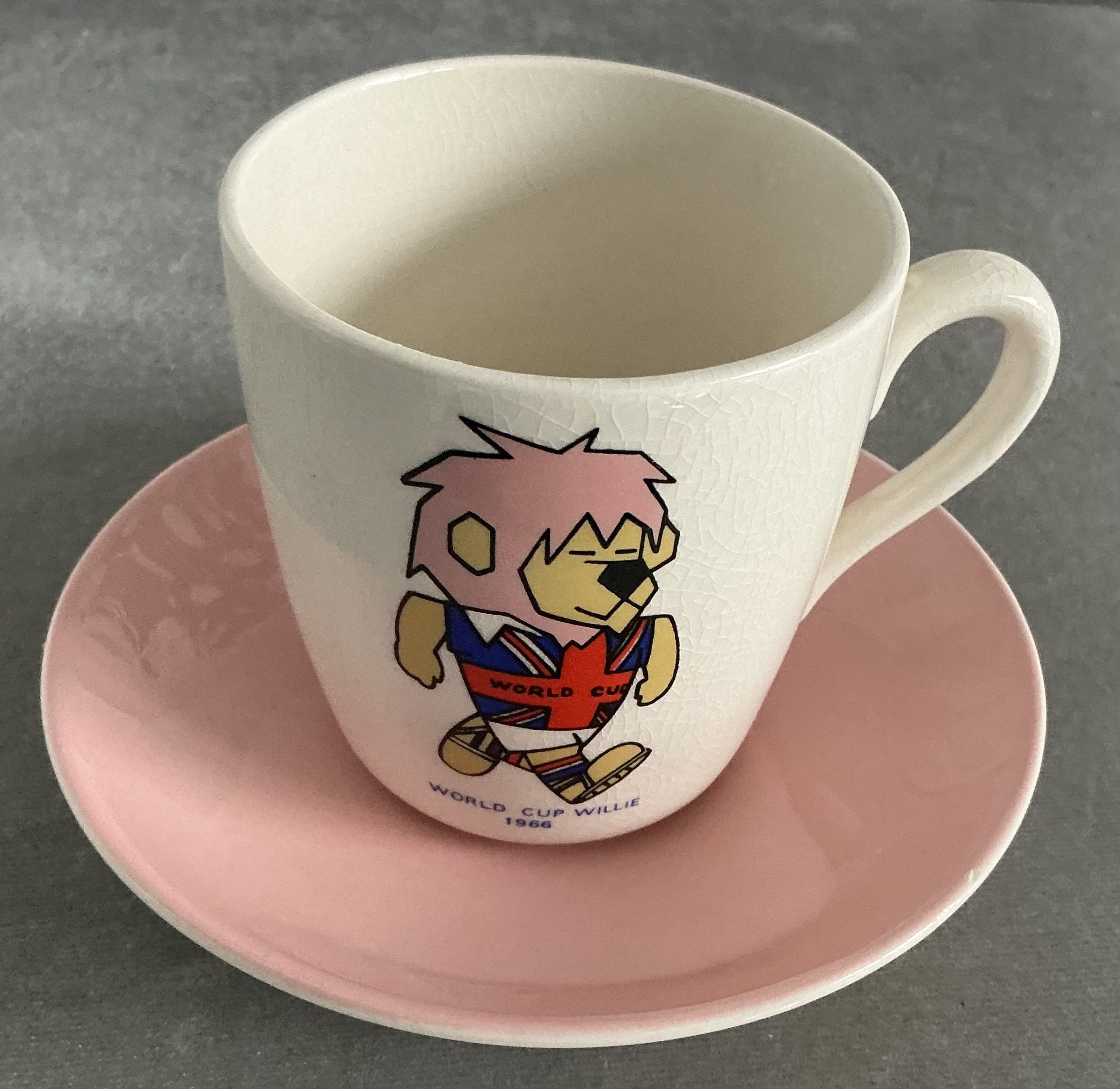 1966 World Cup Willie Tea Cup: Stunning condition featuring a colourful WC Willie cup with handle. Underneath the Football Association copyright. C/W saucer that we are informed belongs with the cup but without FA copyright we are not so certain. (2)