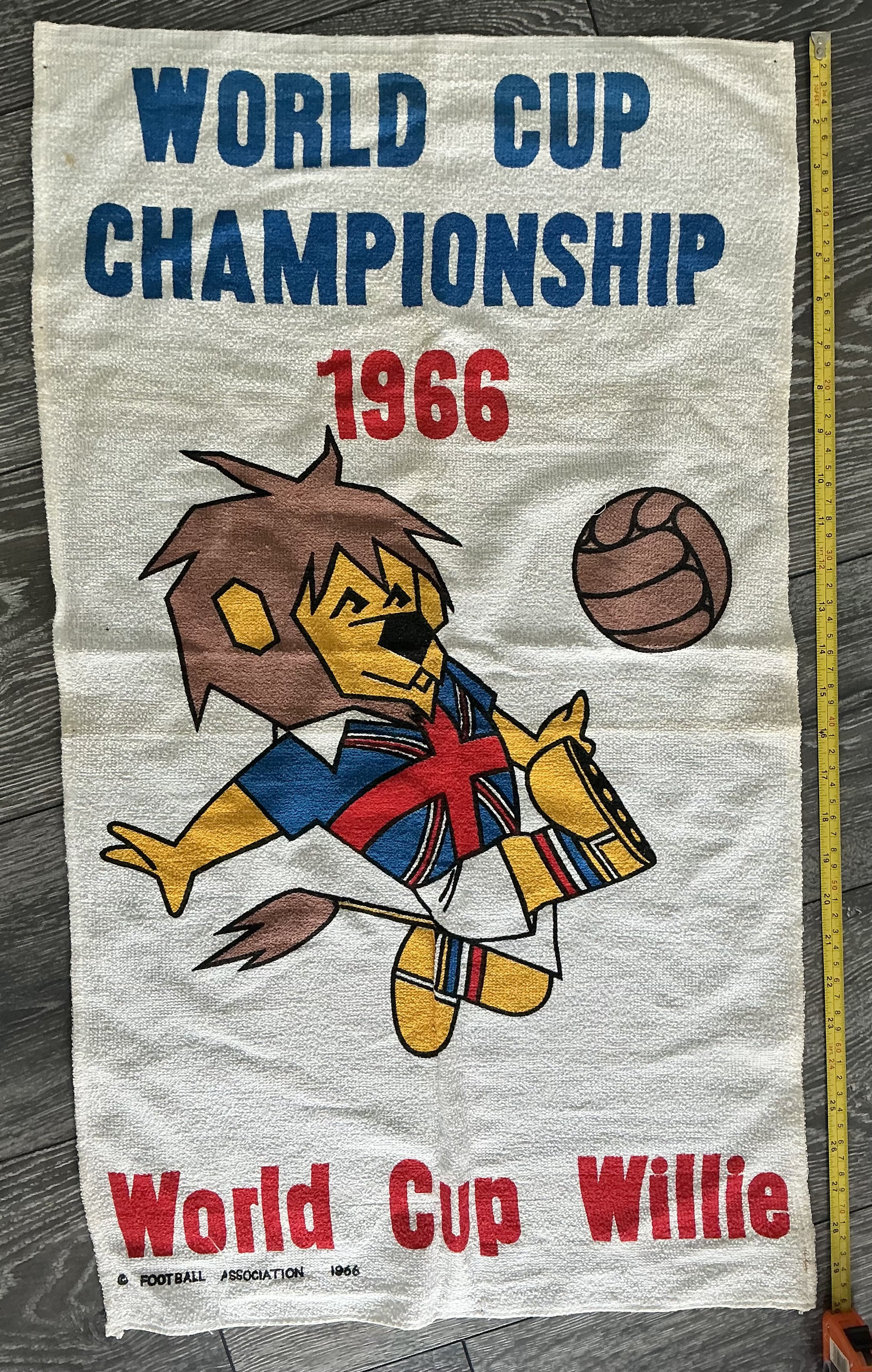 1966 World Cup Willie Hand Towel: World Cup Willie printed underneath Willie with vibrant colours to middle kicking a football. The top reads World Cup Championship 1966. Probably too big for a tea towel so at 30 inches probably a hand towel. FA copyright to bottom. 