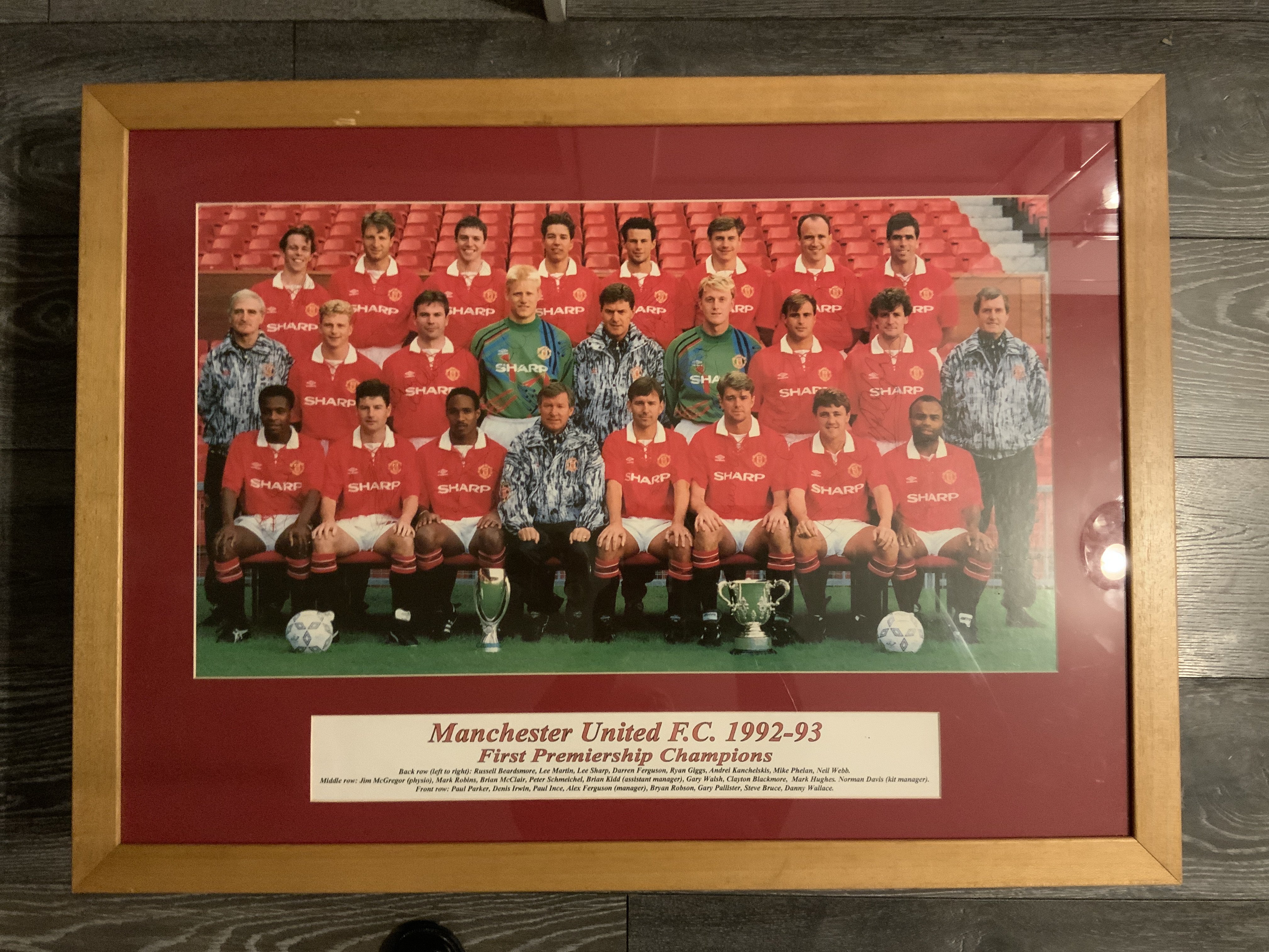 Manchester United Signed Framed 92/93 Premier League Champions Photo: Measuring 32 x 24 inches nicely framed with players identified underneath. There are 25 staff pictured including Alex Ferguson Brian Kidd Kit man and physio. Autographs are in biro so not bold but consistent with the era. Although Ferguson is faint because its blue biro on blue jacket you can see an autograph for 24 of the 25 with only Neil Webb missing. Nice item entitled First Premier Champions. 