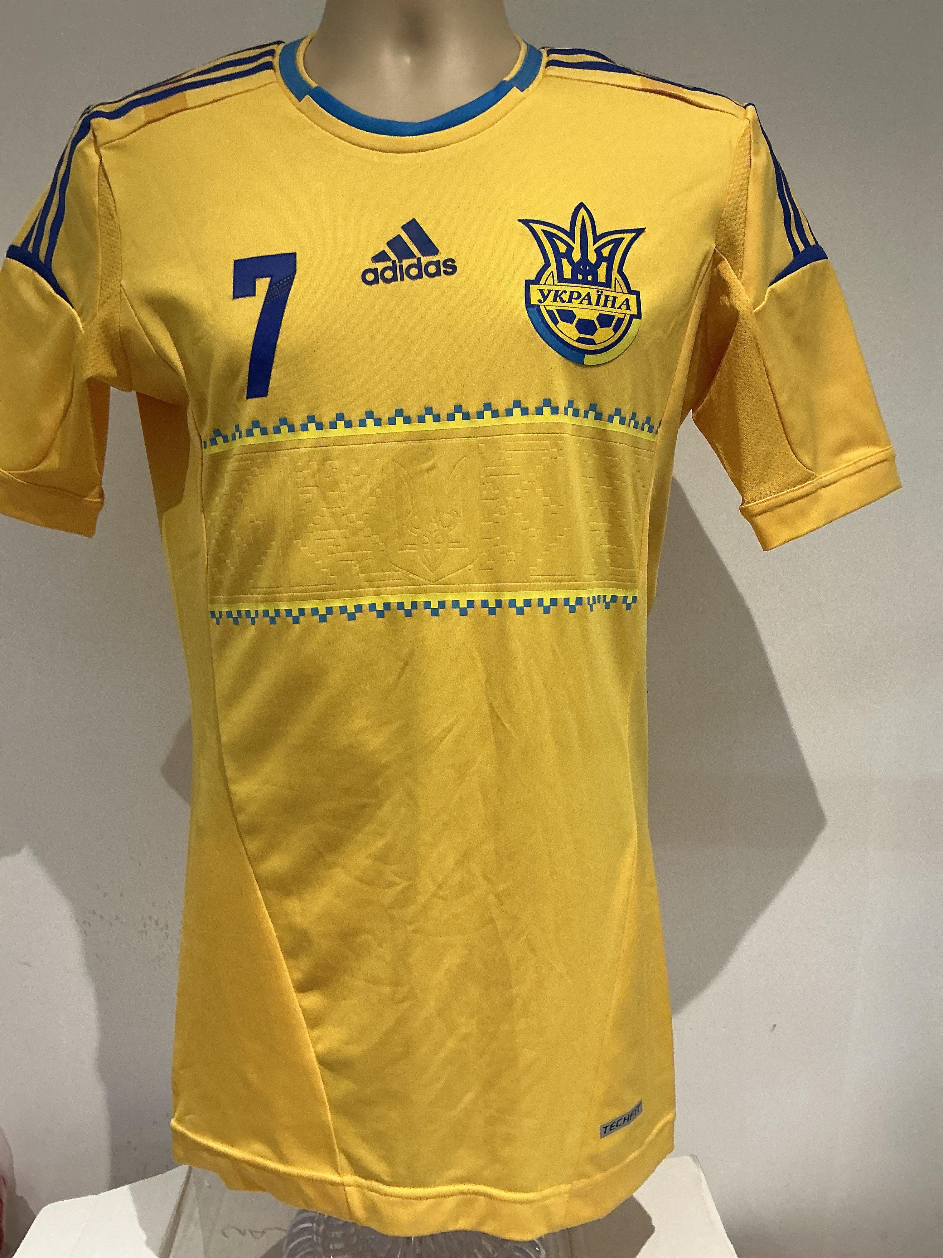 Ukraine 2012 Shevchenko Match Worn Football Shirt: The Adidas yellow 7 short sleeve was worn by the Ukrainian former professional football player Andriy Shevchenko in a friendly match during the 2012 season with his national team. Shevchenko is considered one of the greatest strikers of all time and Ukraines greatest ever player. He is the all-time top scorer for the Ukraine national team with 48 goals. The shirt features the name Shevchenko and 7 applied on the back. A smaller 7, Adidas logo, and the National Team crest are applied on front. Two pairs of adidas blue stripes are applied on the shoulders. The jersey has a unique white rubber band around the lower hem. Sized Medium.
