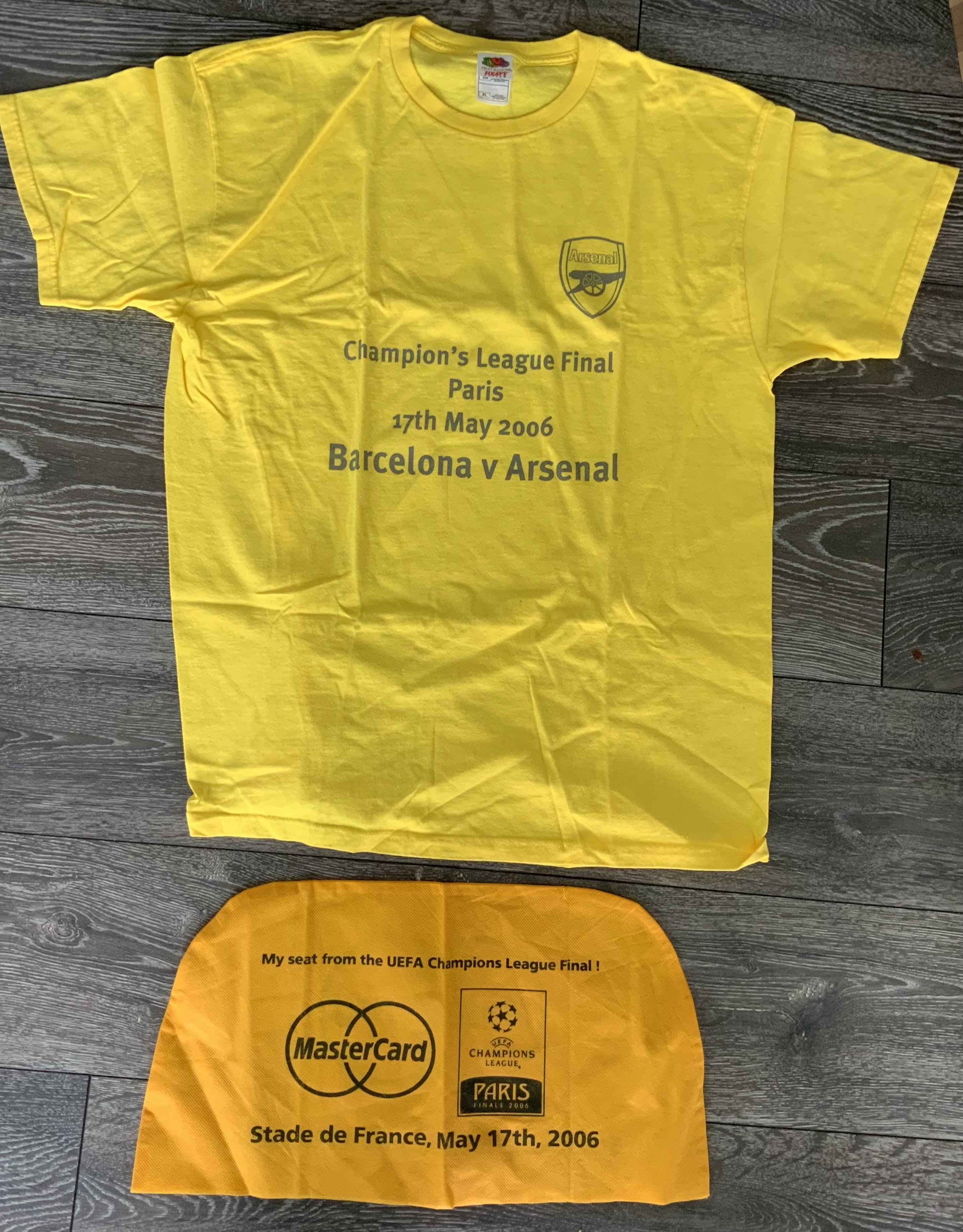 Arsenal 2006 Champions League Football Memorabilia: Removed from seat when entering the stadium and unused. Yellow XL t shirt with Arsenal badge and match details to front. C/W a seat cover with venue and date sponsored by Mastercard. (2)
