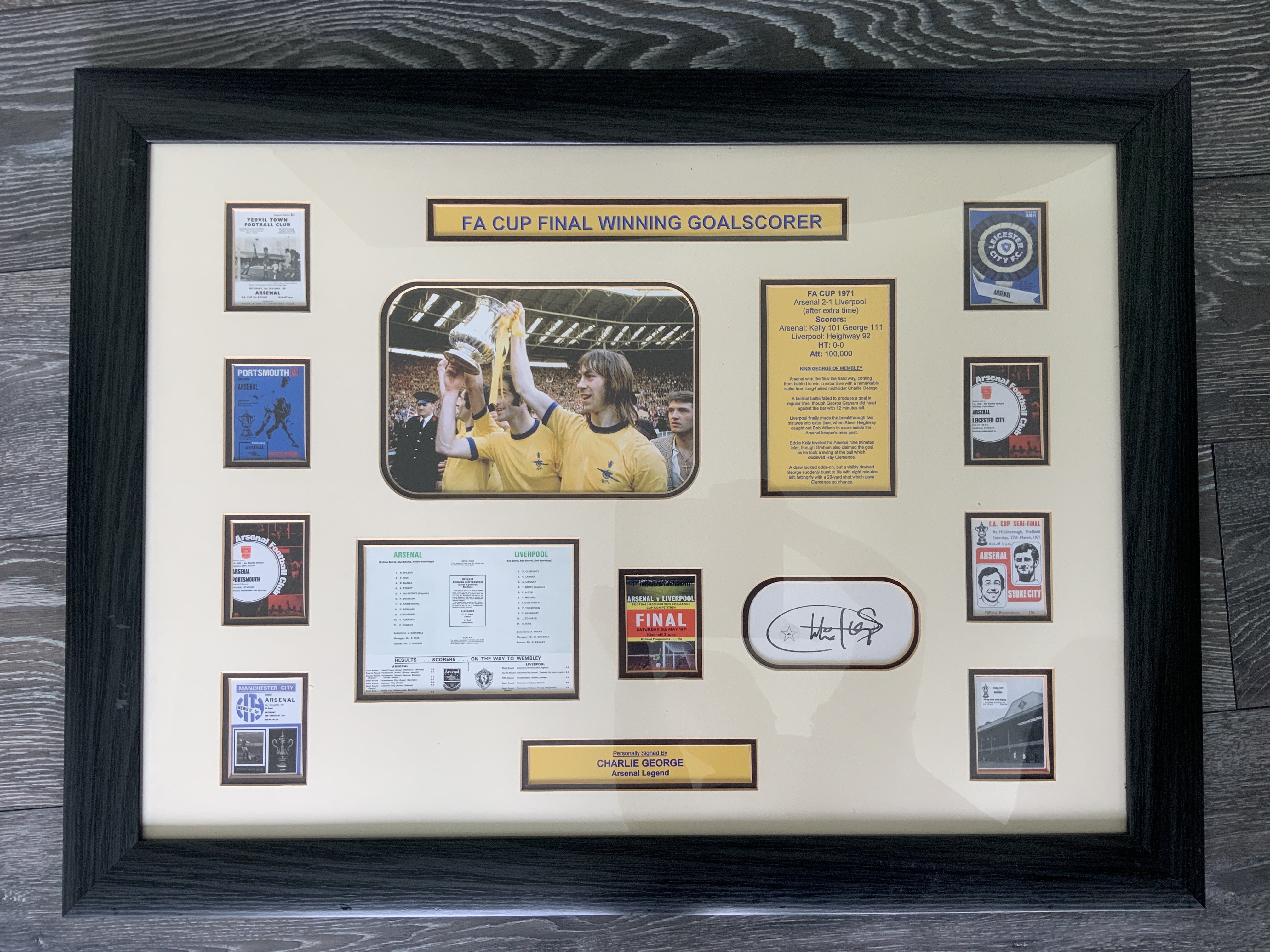 Arsenal 1971 FA Cup Final Signed Framed Football Display: A miniature reprint of the programme covers from every game in the FA Cup winning run. In this expensively framed montage is a picture of winning goalscorer Charlie George and also his autograph. Attractive piece measuring 31 x 24 inches. COA to rear.