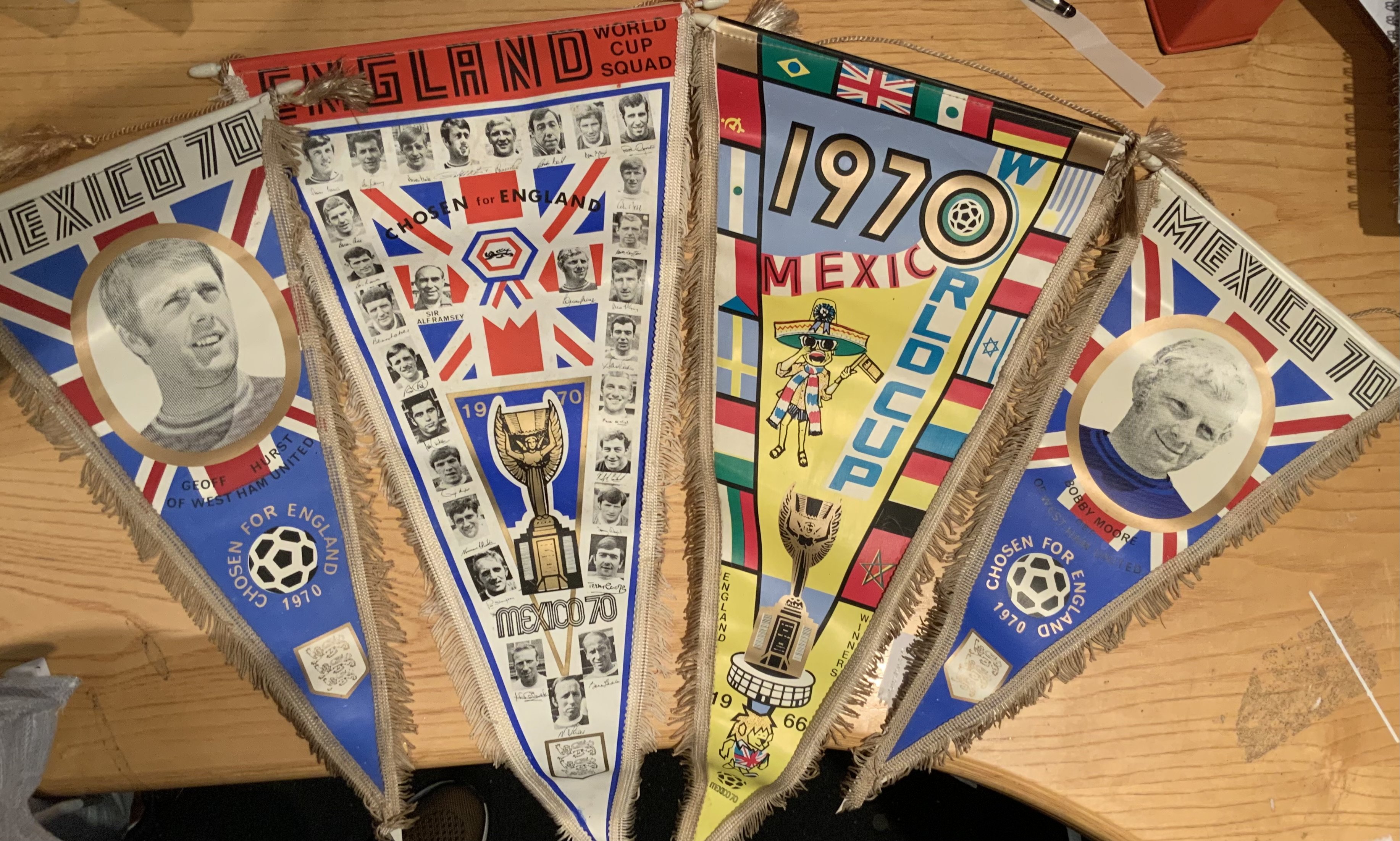 1970 England World Cup Football Pennants: 20 inch original pennants one featuring the England World Cup squad with the participating other nations flags. Two others which are 16 inches feature Hurst and Moore. 3 are made by Coffer. Excellent. (4)