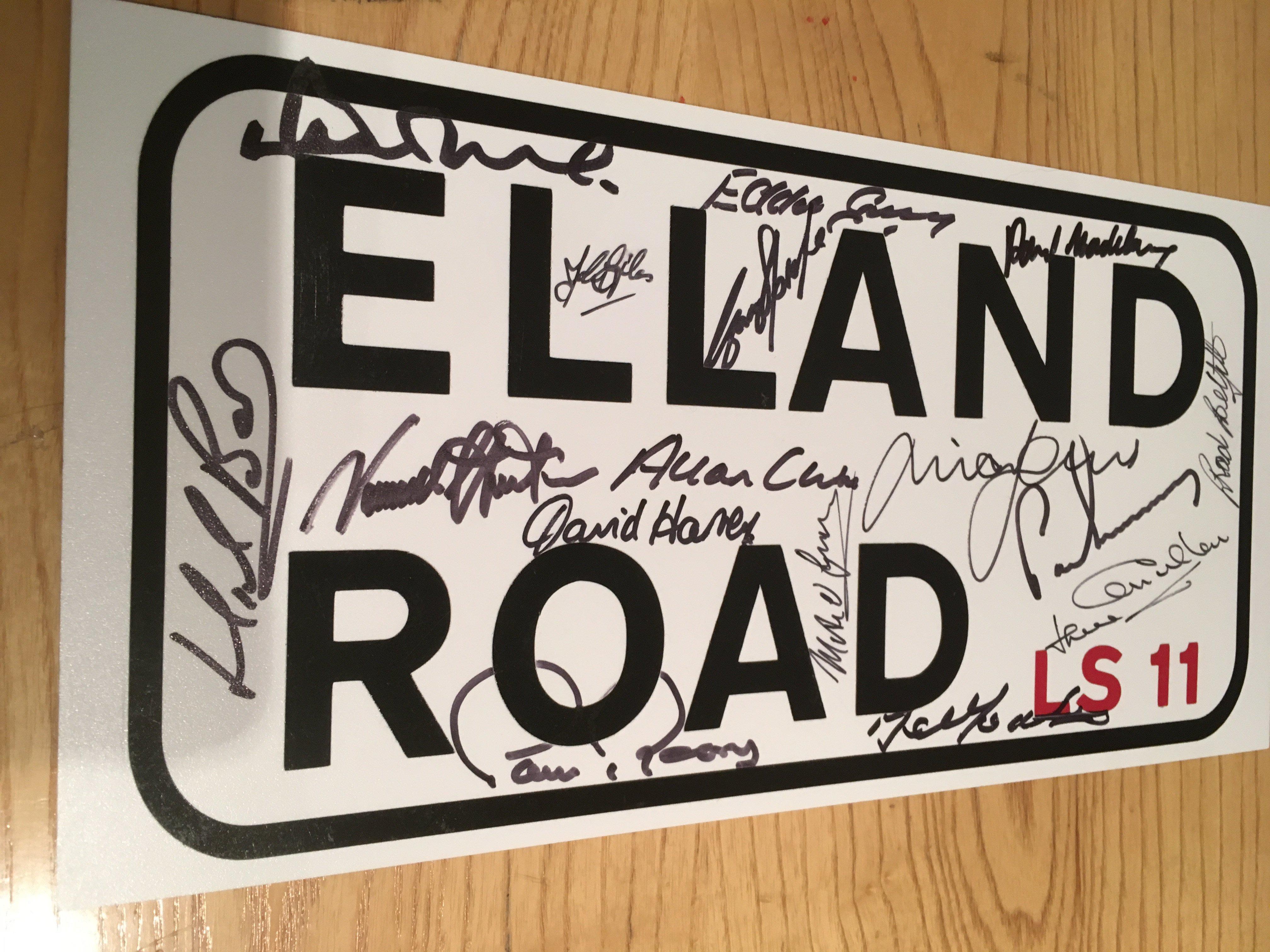 1970s Leeds United Signed Elland Road Sign: Replica 13 inch road sign signed by legends Reaney Gray Hunter Jones Clarke Harvey Charlton OGrady Madeley Bates Lorimer Giles Sprake McKenzie Yorath and Belfitt. Coa from reputable source.