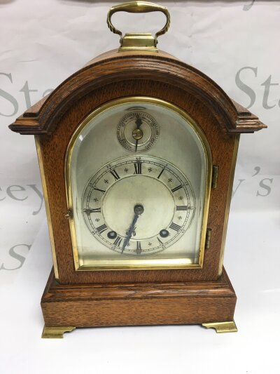 An oak cased 8 day mantel clock with Roman numerals on a silvered dial, approx heigh 30cm.