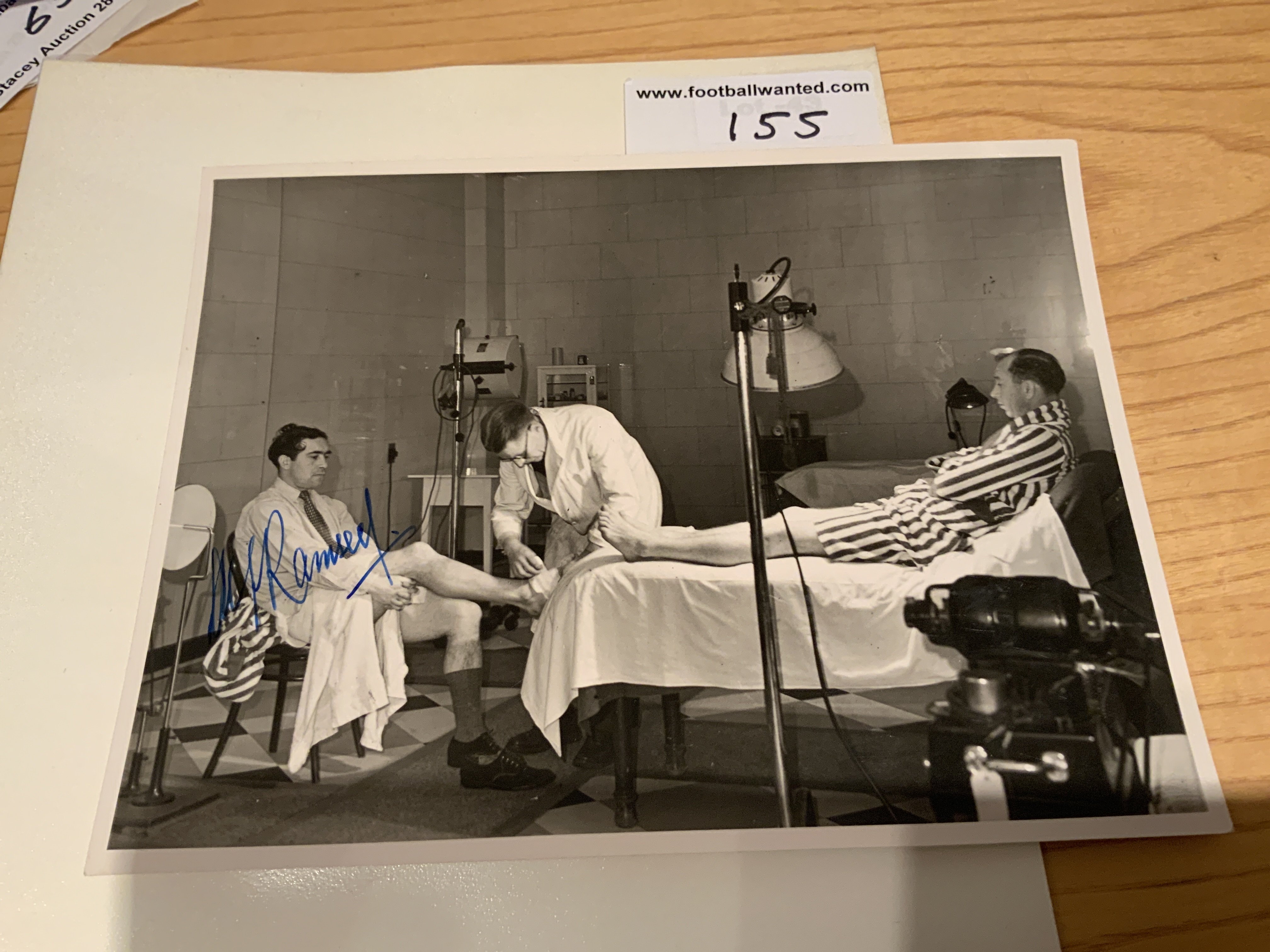 Alf Ramsey Tottenham Signed Football Press Photos: Superb photo depicting Ramsey receiving treatment in the treatment room with Ron Burgess on the bed awaiting his treatment. Signed clearly without dedication by Ramsey. Press stamp to rear.