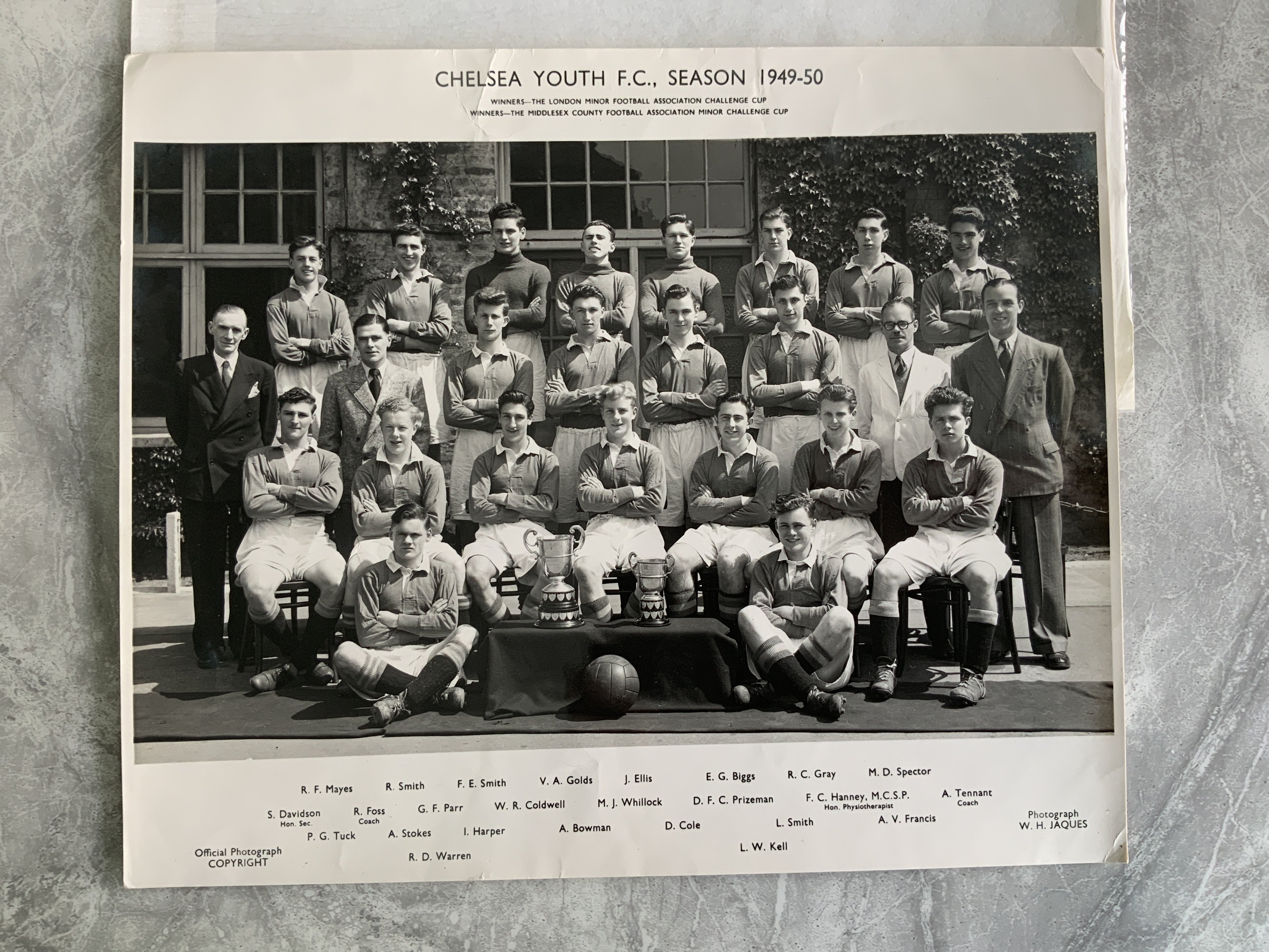 Old Chelsea Youth Team Official Football Photos: 10 x 12 inch club photo by Jaques picturing the 49/50 youth team with 25 players all named under the two cups they had won. C/W the 60/61 Youth Cup winners on original photo pictured with 3 cups. All players named on separate sheet. Press photos on old paper without press stamps. (2)