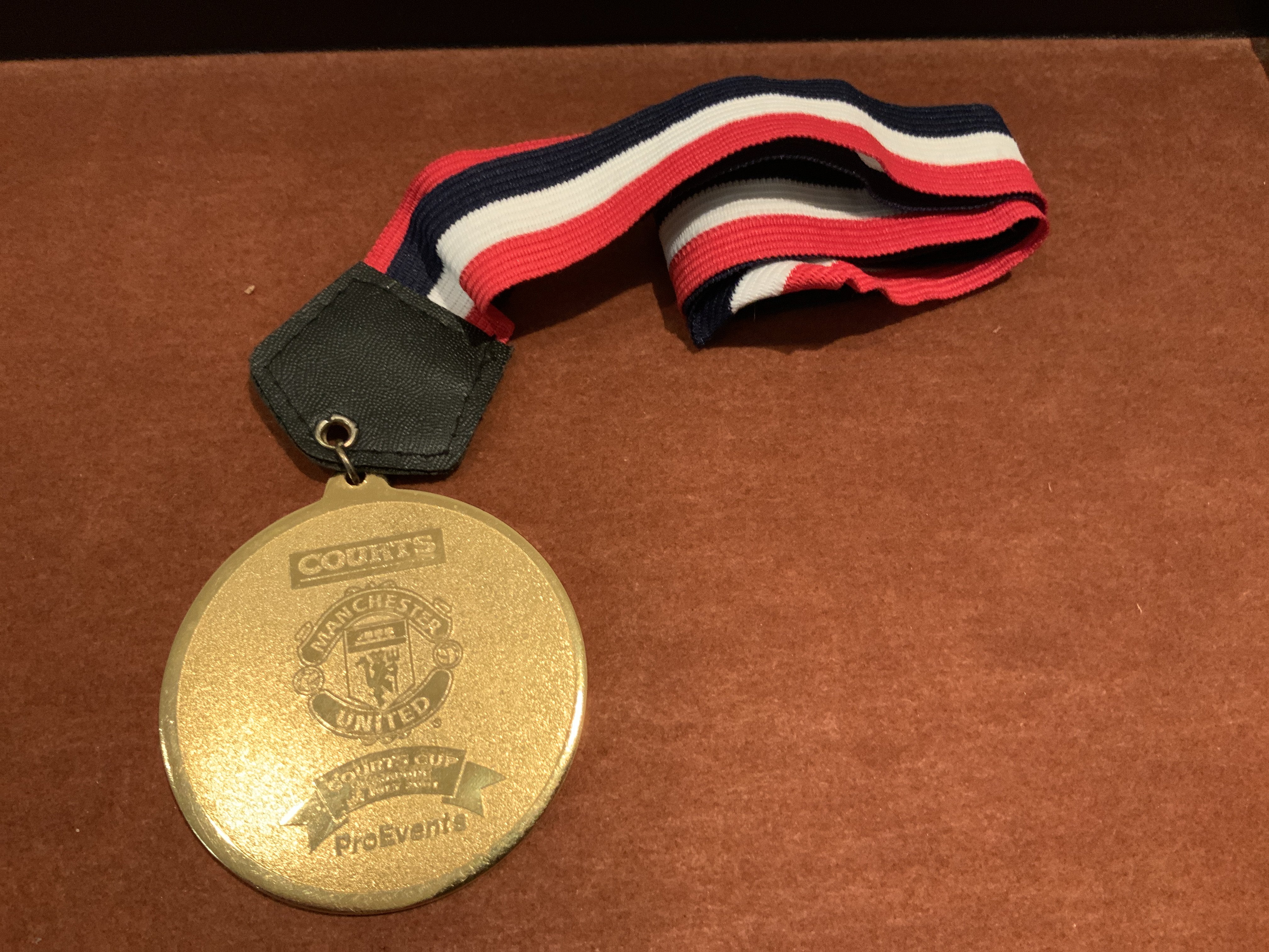 2001 Singapore X1 v Manchester United Players Medal: Large gold coloured medal with Manchester United badge and the words Courts Cup Singapore 24 7 2001. The reverse has the words Champions. Red white and black lanyard attached. Awarded to a Manchester United player.