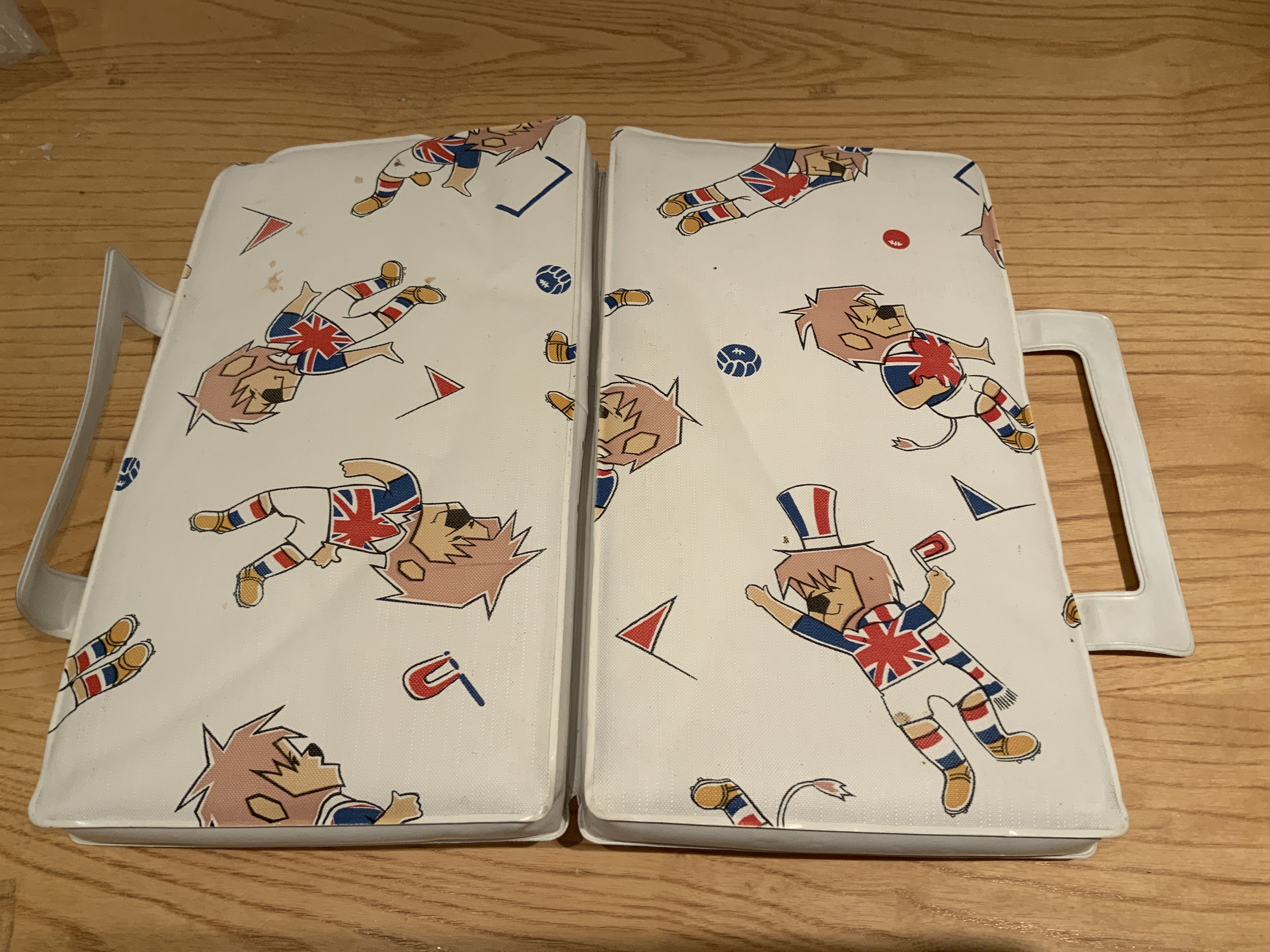 1966 World Cup Willie Seat Cushion: Folded cushion used to pad the wooden Wembley Stadium seats at the World Cup. Intended to be carried into the stadium with handle intact.
