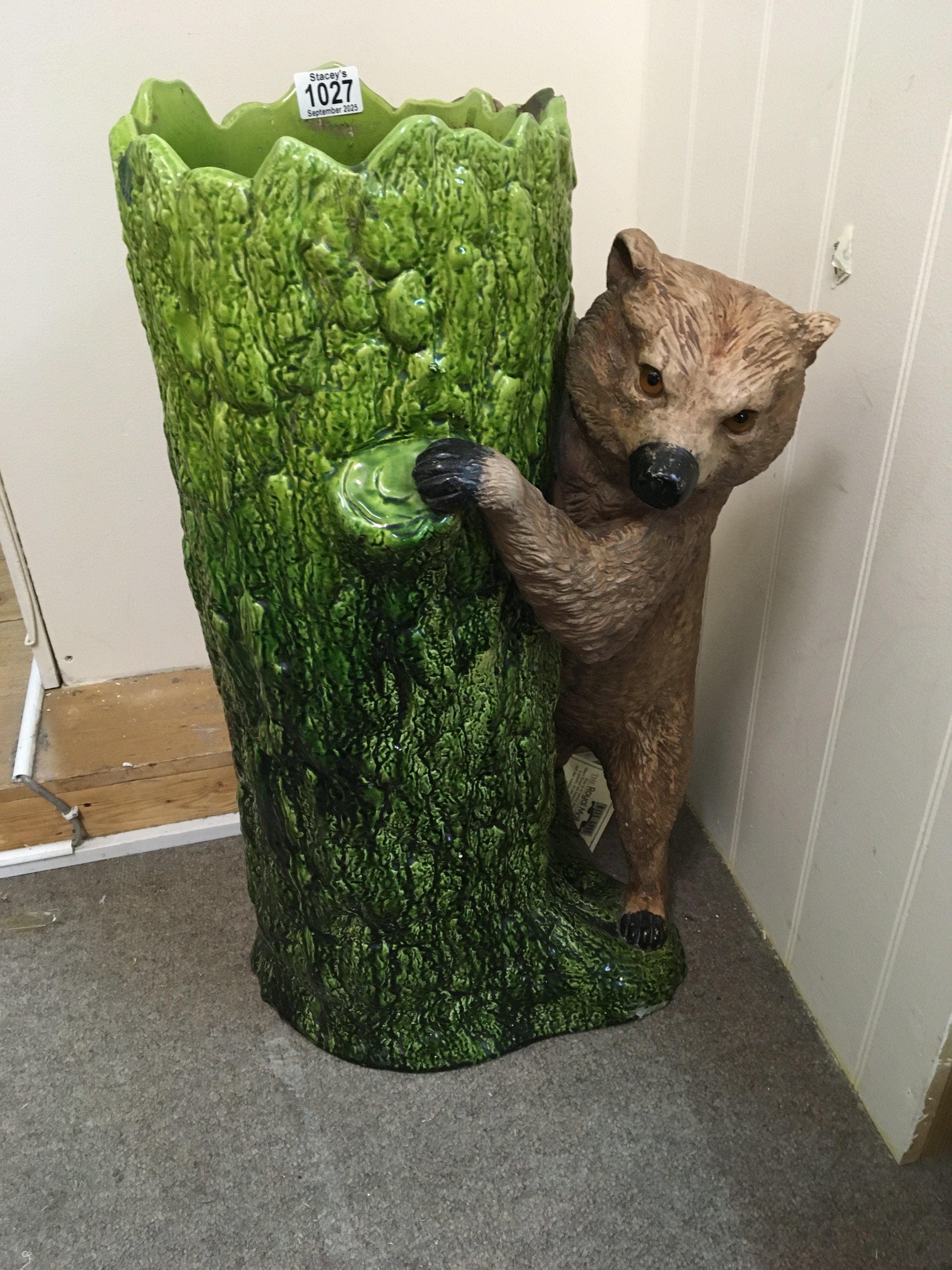 A Bretby stick stand in the form of a bear beside a tree trunk .