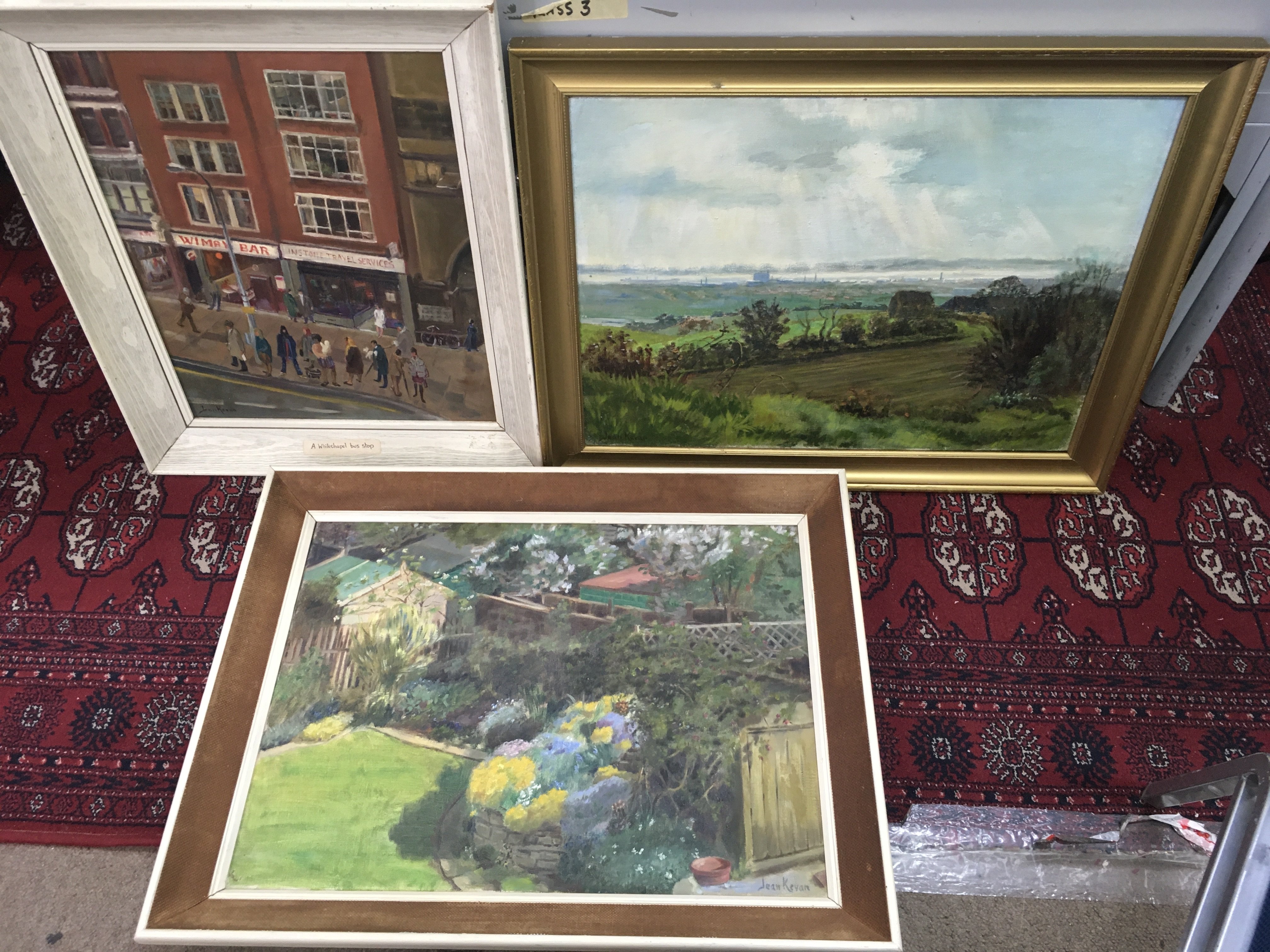 Three framed Jean Kevan (1916-2006) oil on canvas paintings including a street view of a Wimpy Bar in Aldgate East London 1970s, view of the Thames Estuary from Benfleet and a garden scene. Frame size dimensions 72x56cm & 52x61cm