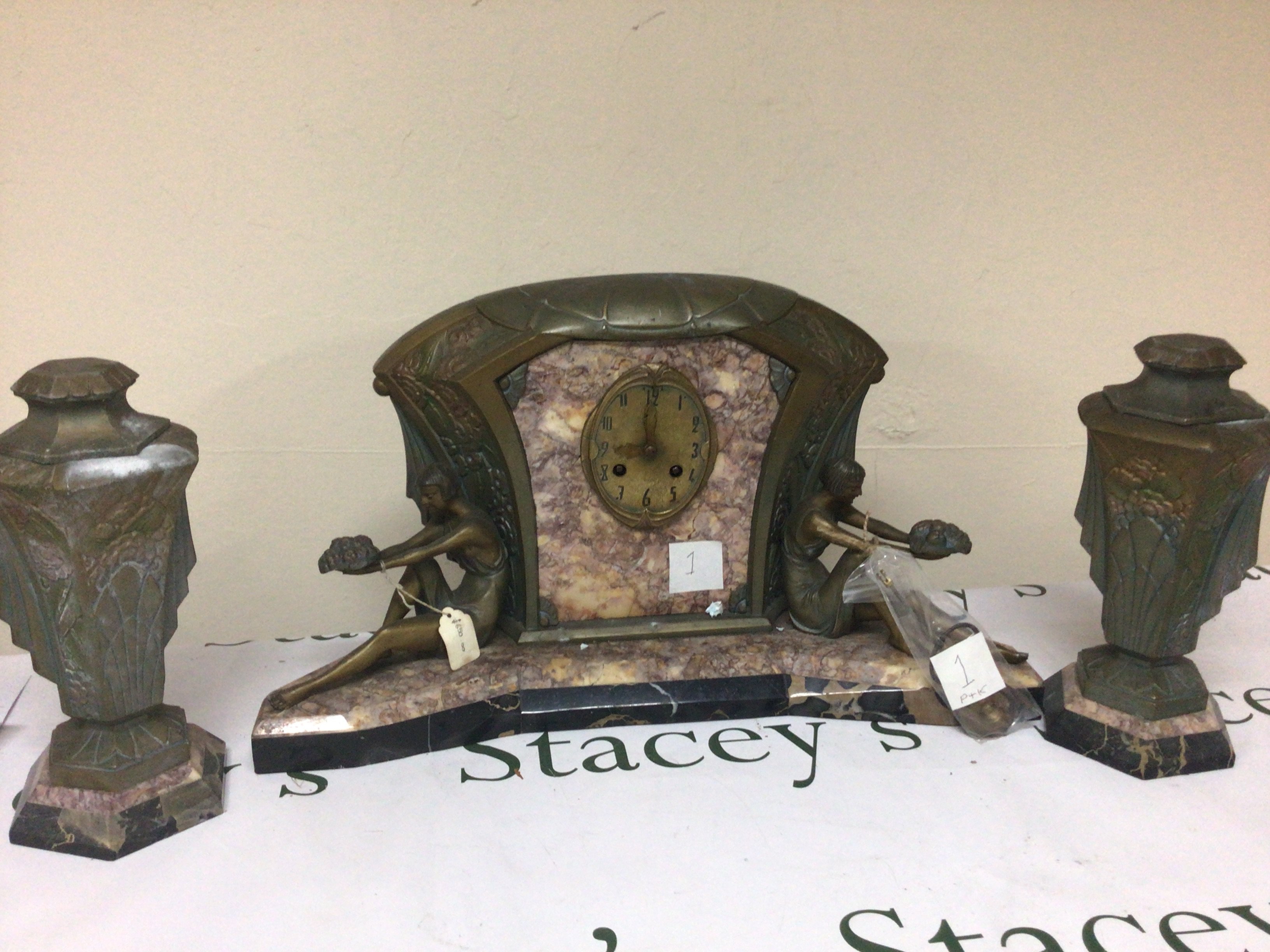 An Art Deco clock garniture the clock with Brocatelle and patterned black marble with coloured metal mounts flanked by two reclining female figures.with matching side ornaments. With key and pendulum. The movement striking on a bell.