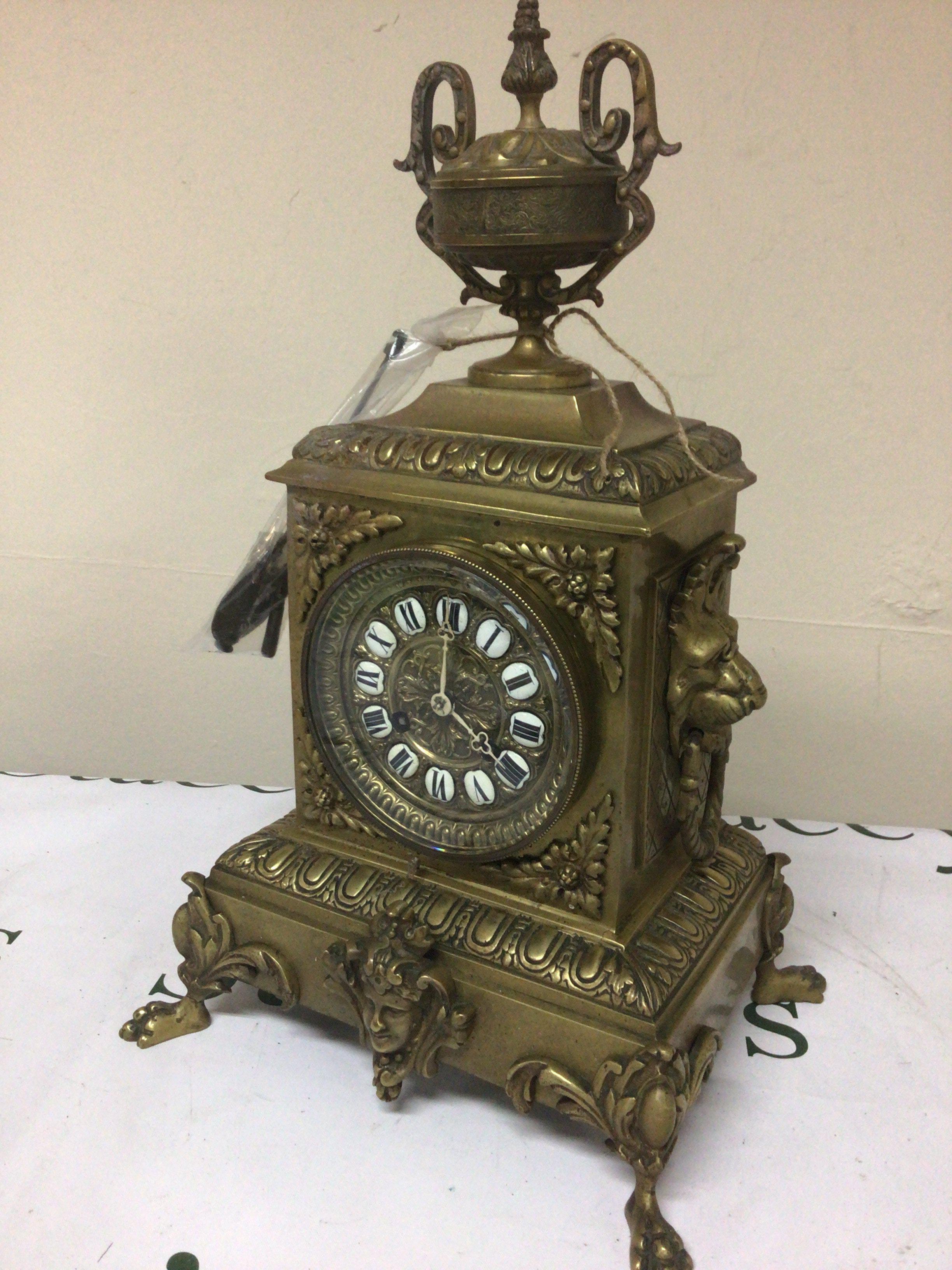 A brass cased late 19th century French clock the case surmounted with loin masks and ring ornamentation and surmounted with a classic urn. With side ornaments key and pendulum. Height 42cm