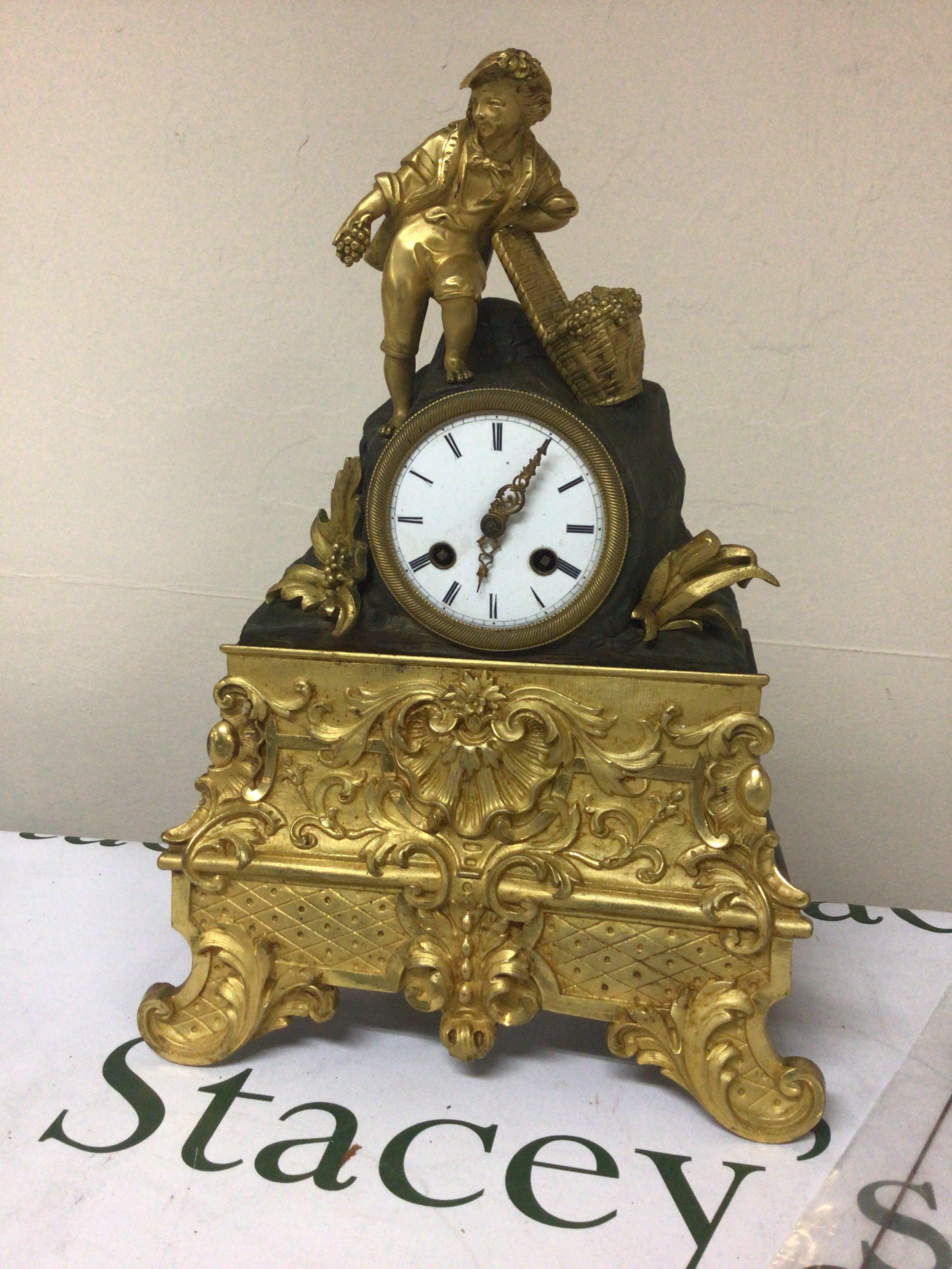 A French late 19th century gilt metal mantel clock the case surmounted with a figure with a basket of grapes the lower section with folate scrolls. Silk suspension movement with pendulum. Height 35cm