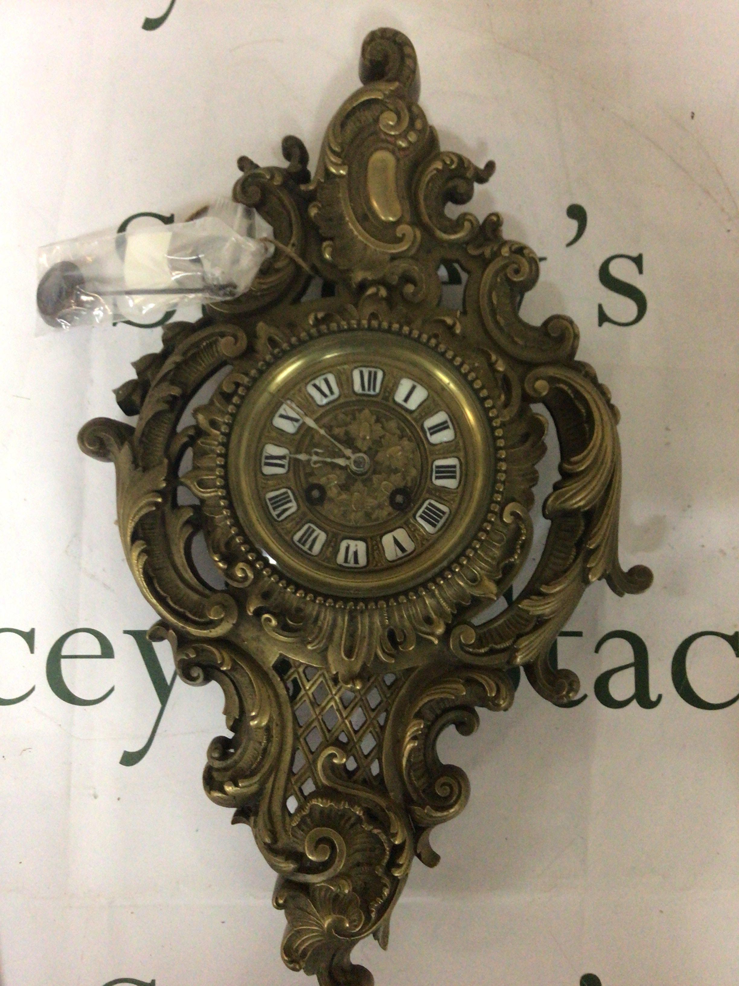 A French brass early 20th century wall clock with elaborate scrolls with key and pendulum 48cm approximately.