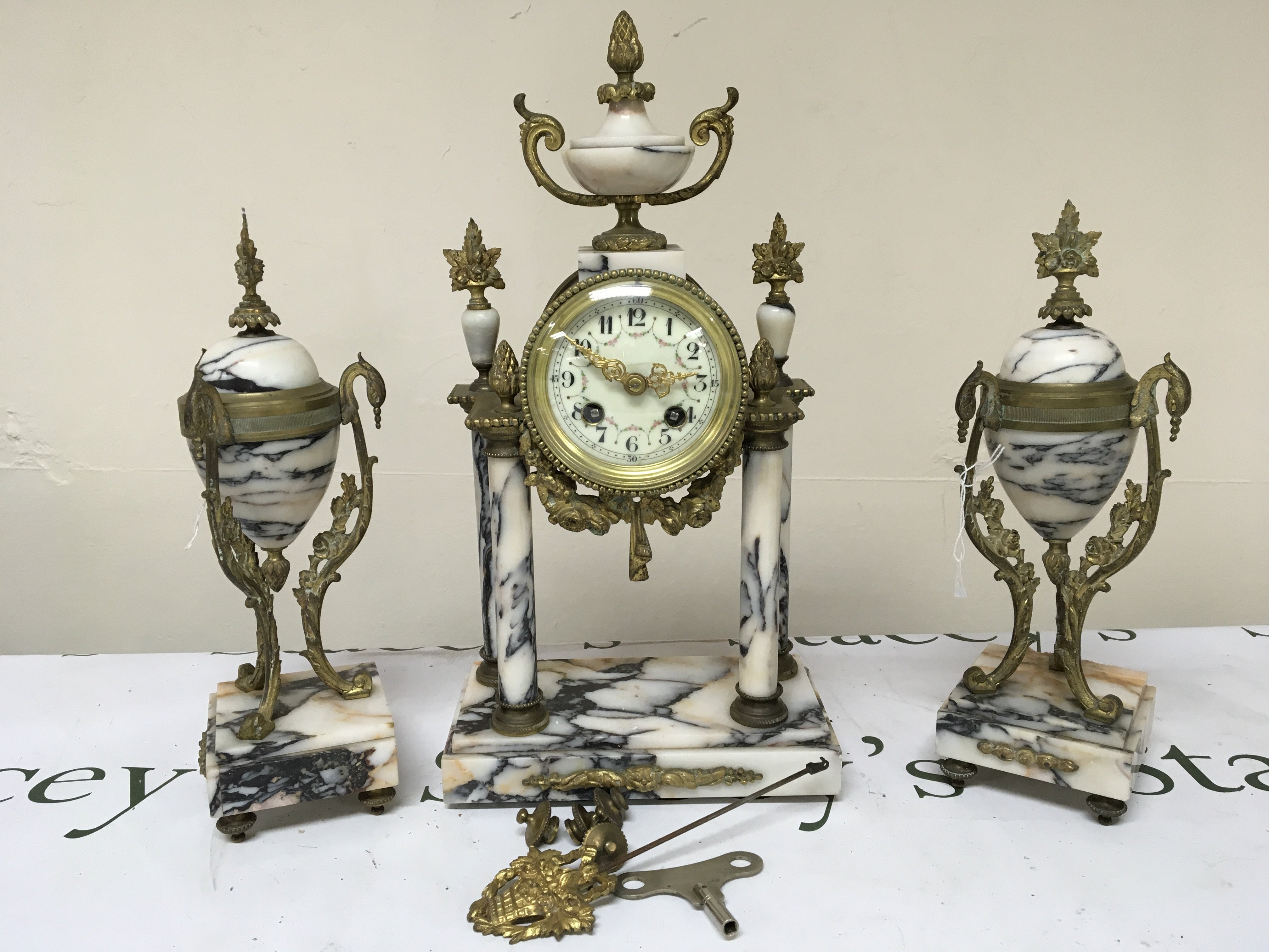 A French late 19th century marble clock garniture of Neo classical design with gilt metal mounts the four pillar clock with an enamel dial with key and pendulum and small feet. 40cm height.